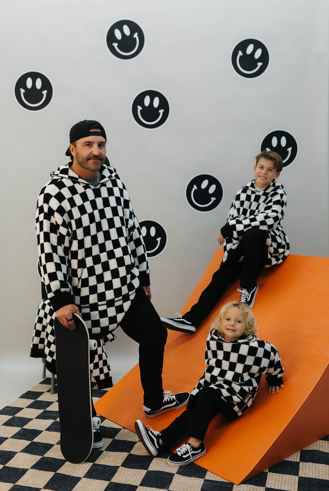 Two adults and a child in matching checkered outfits on an orange platform with smiley face patterns.