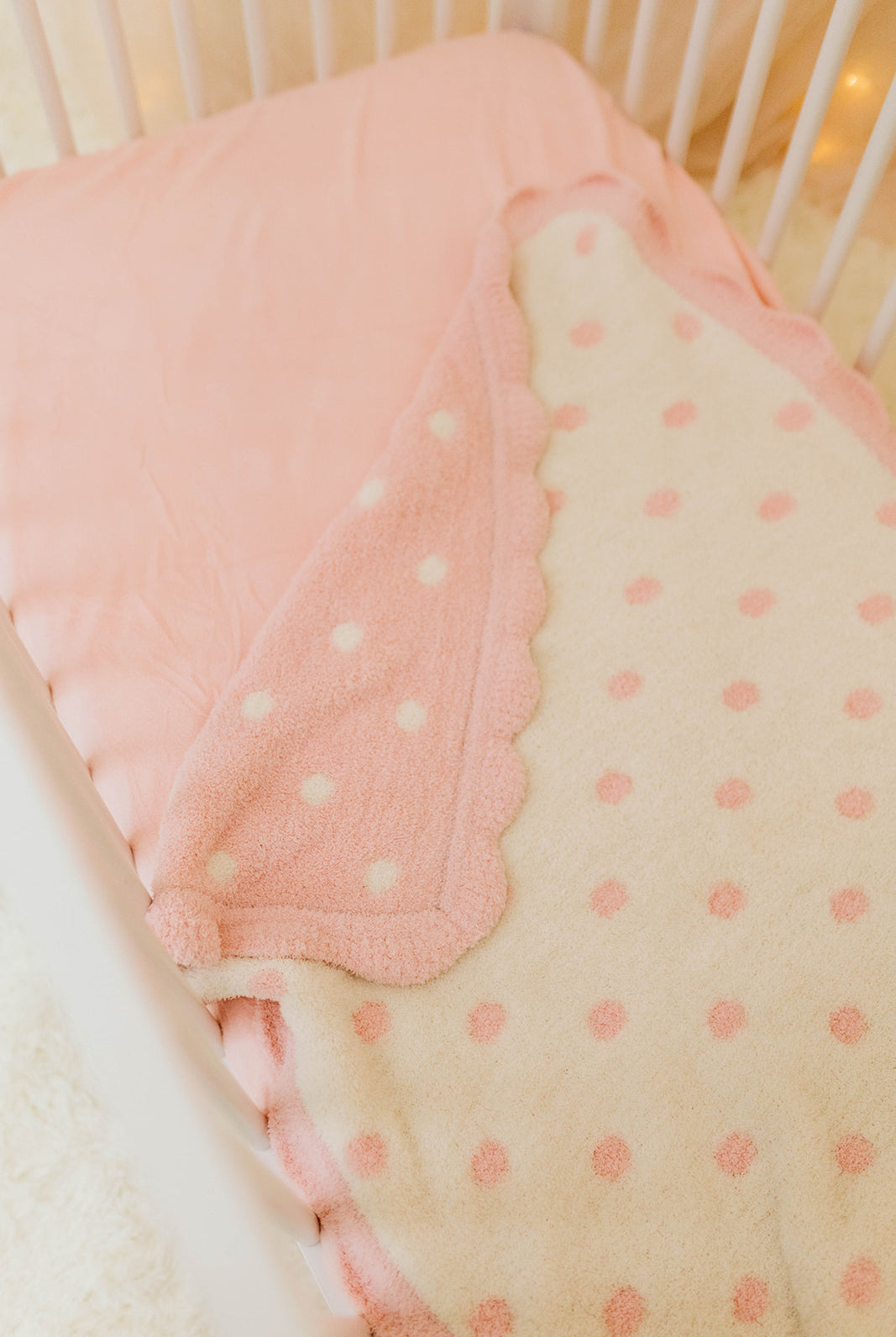 Pink and beige polka dot crib bumper with white crib in the background