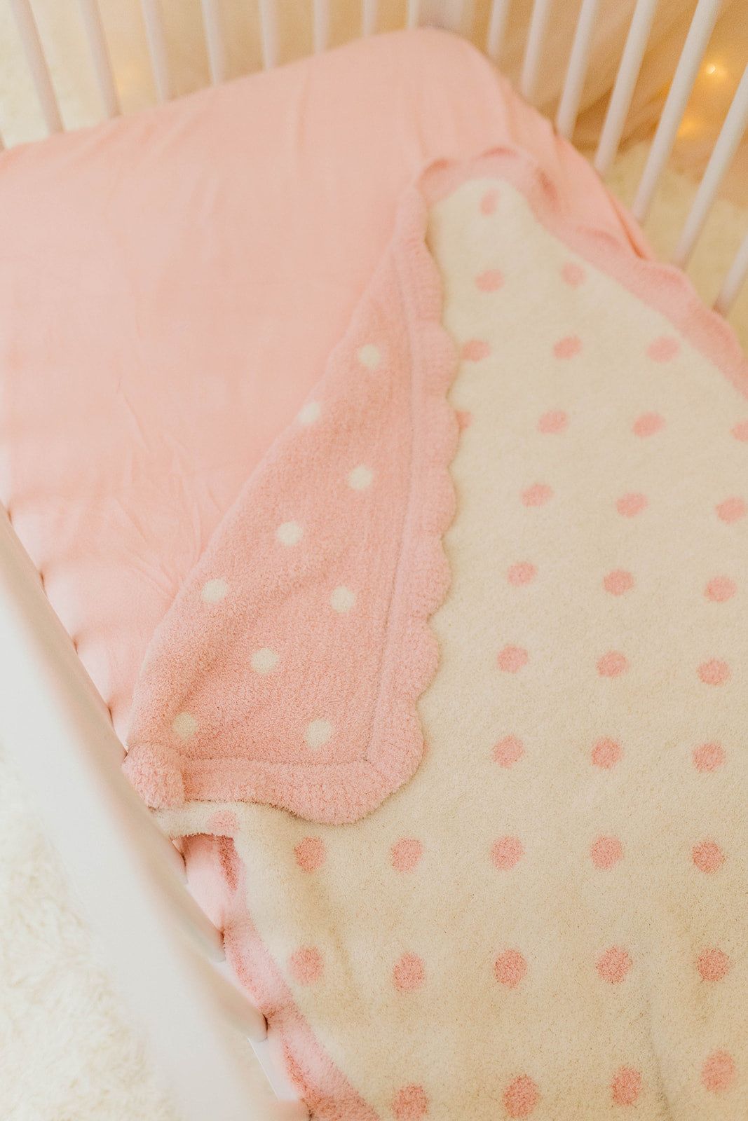 Pink and beige polka dot crib bumper with white crib in the background