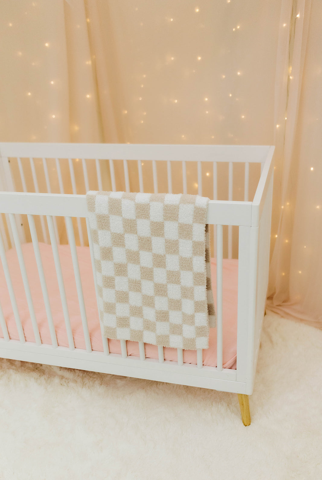 White crib with sand and white checkered blanket against a softly lit curtain background