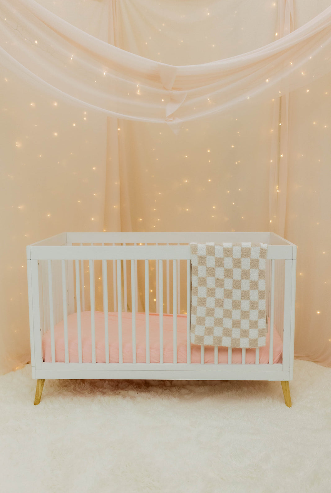 White crib with checkered blanket in a softly lit room