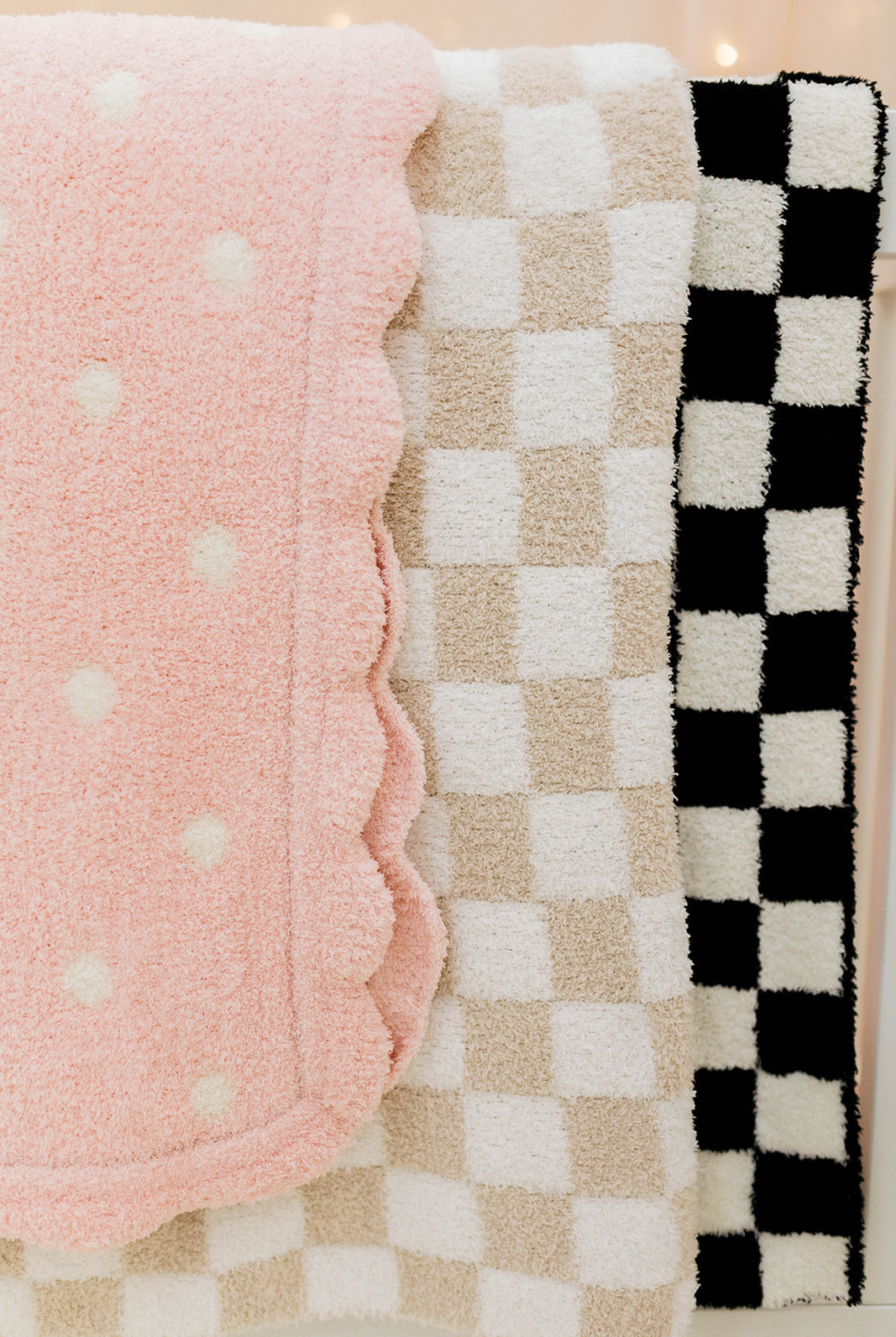 Three textured baby blankets in pink with white polka dots, beige checkered, and black and white checkered patterns.