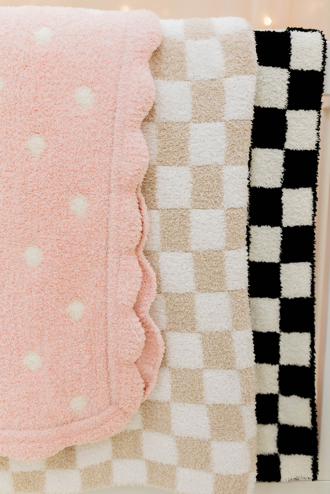 Three textured baby blankets in pink with white polka dots, beige checkered, and black and white checkered patterns.