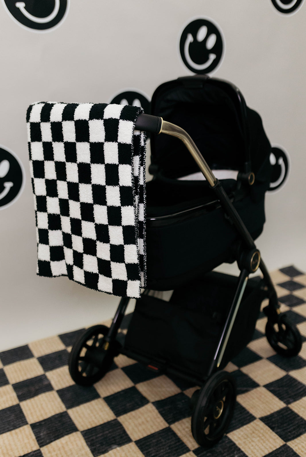 Black and white checkered blanket draped over a black stroller on a checkered floor.