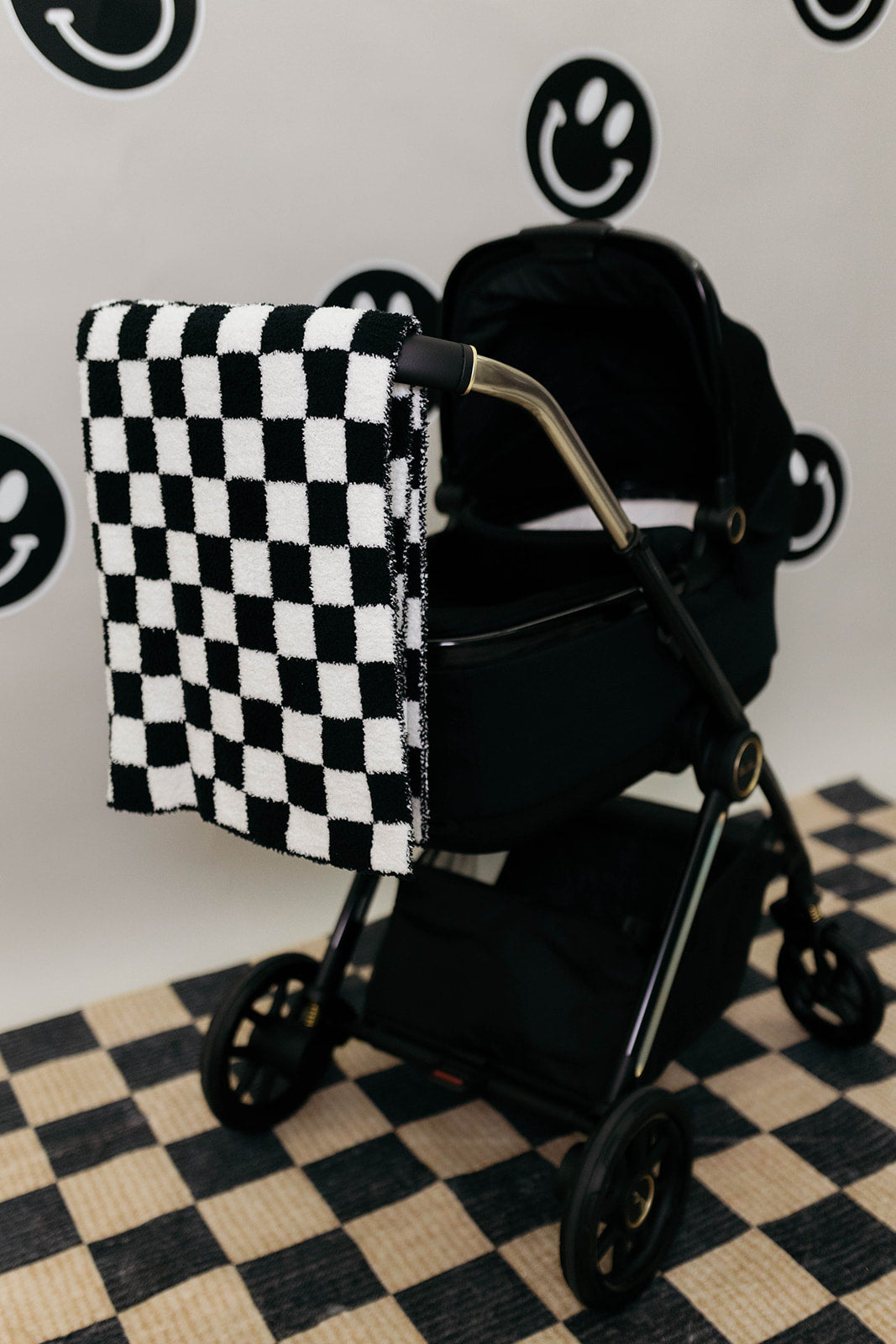 Black and white checkered blanket draped over a black stroller on a checkered floor.