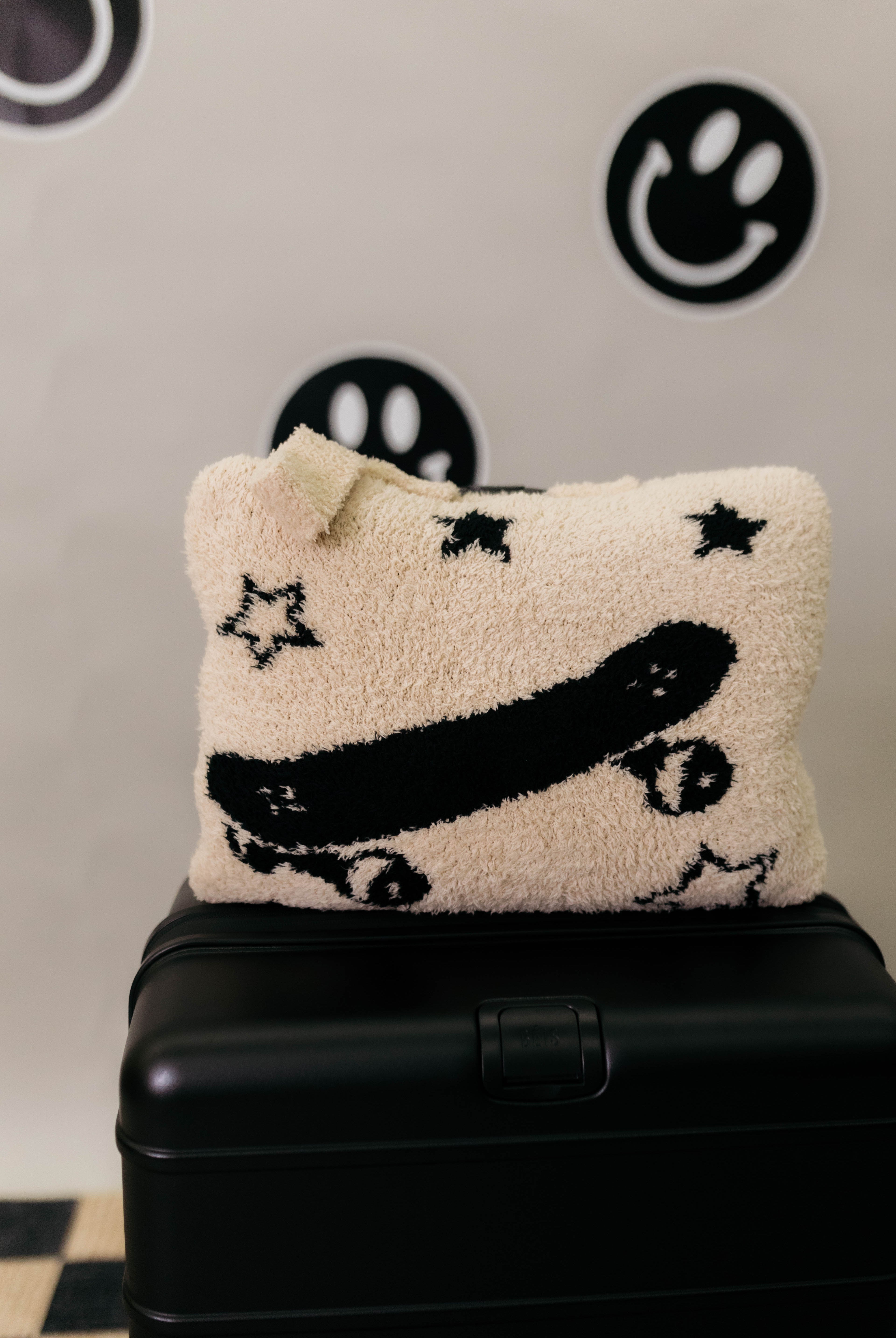Decorative quillow with star and skateboard design on a black suitcase against a wall with smiley face designs.