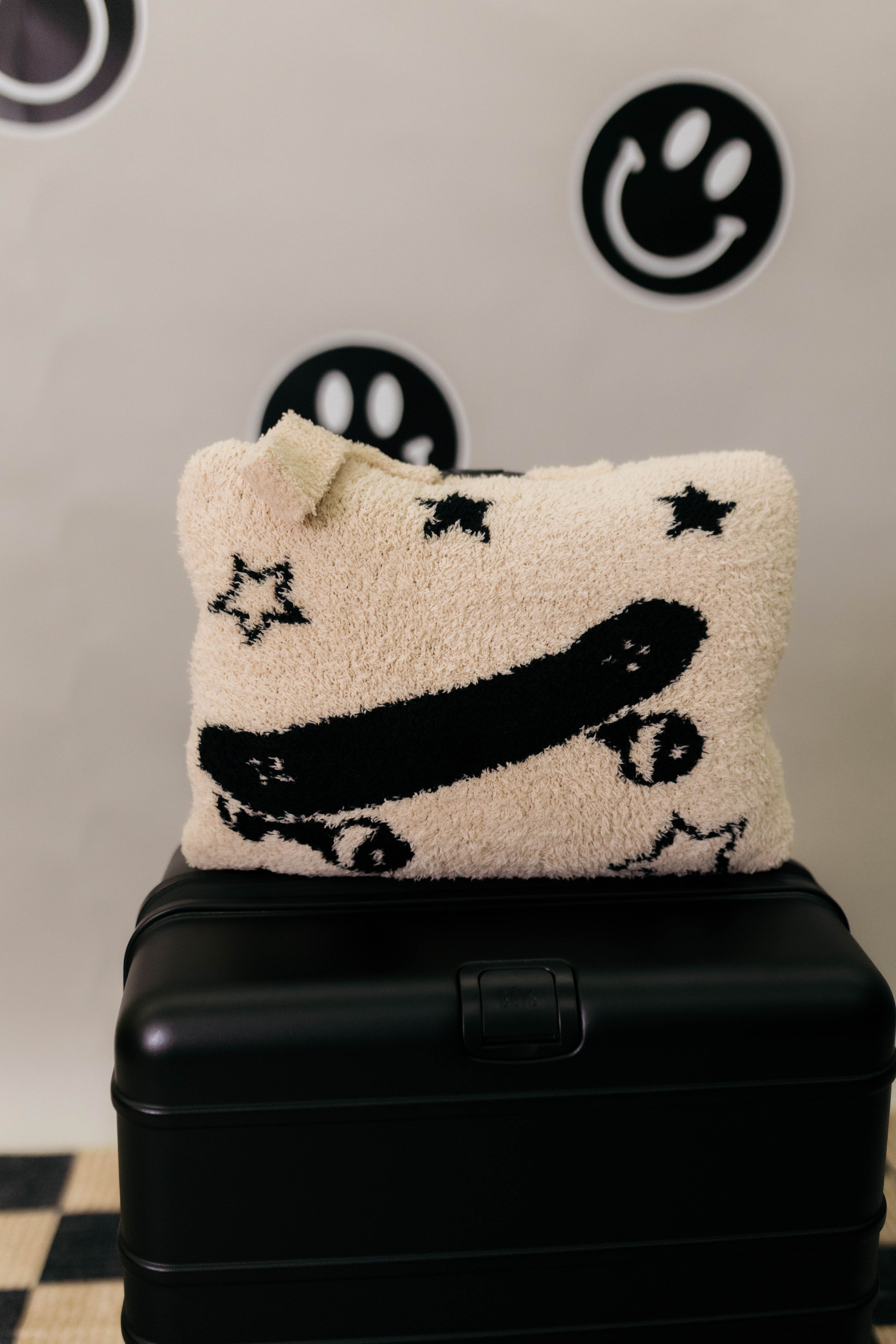 Decorative quillow with star and skateboard design on a black suitcase against a wall with smiley face designs.