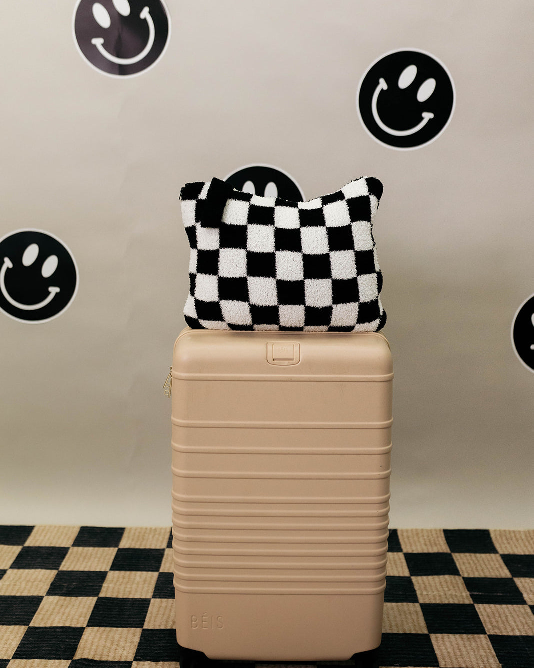 Beige suitcase with a checkered quillow on top against a wall with smiley face stickers.