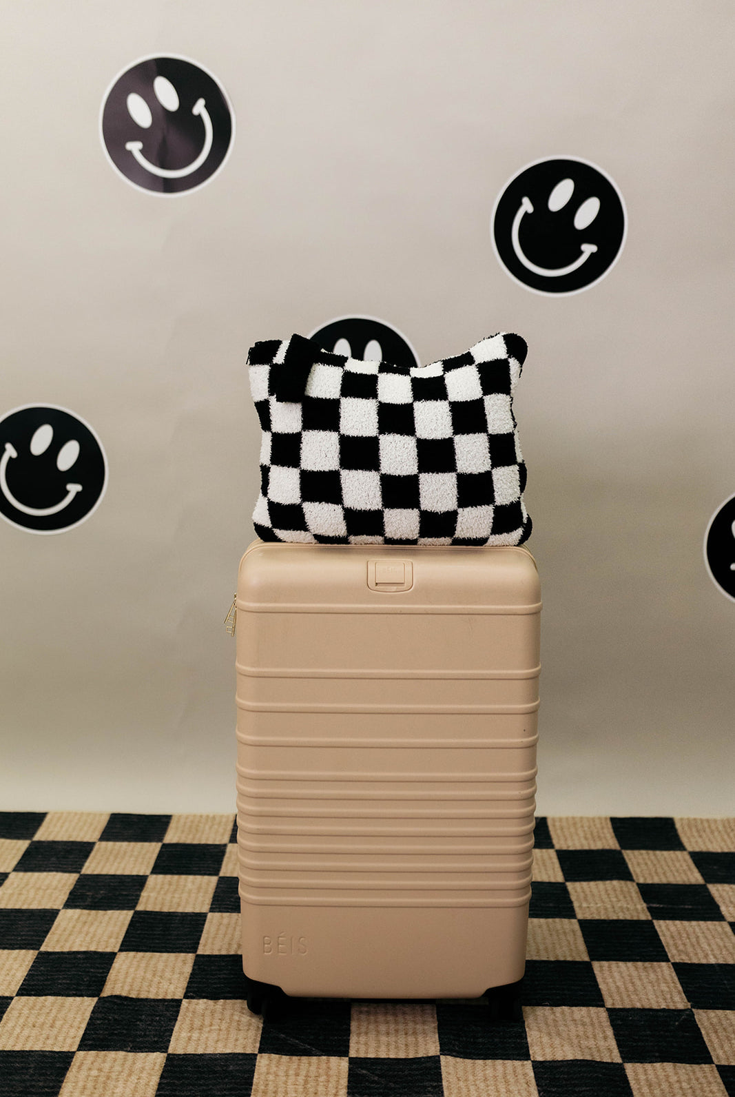 Beige suitcase with a checkered quillow on top against a wall with smiley face stickers.
