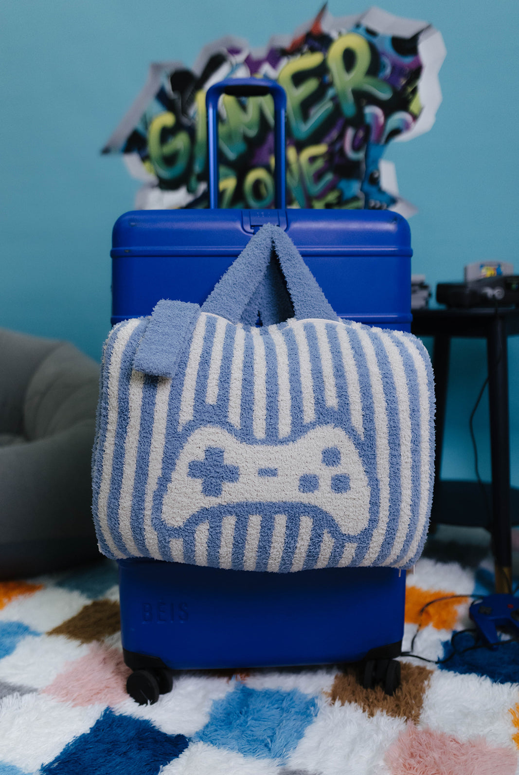 Blue suitcase with a striped quillow featuring a game controller design on a colorful rug.
