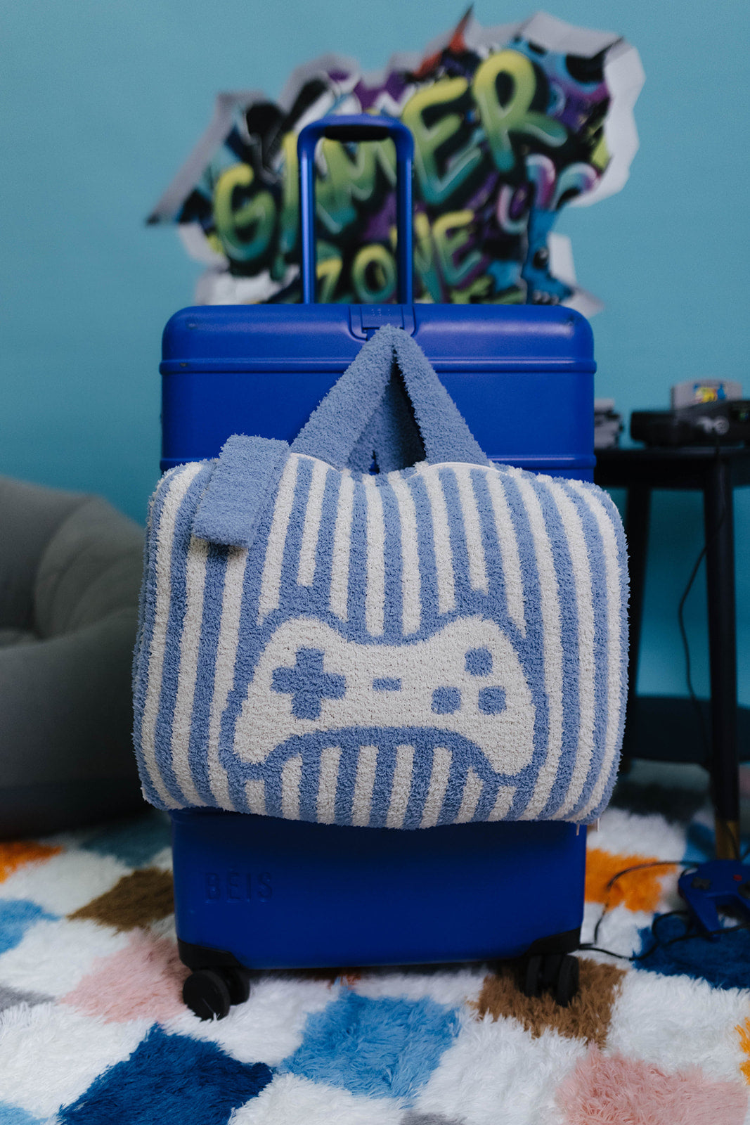 Blue suitcase with a striped quillow featuring a game controller design on a colorful rug.