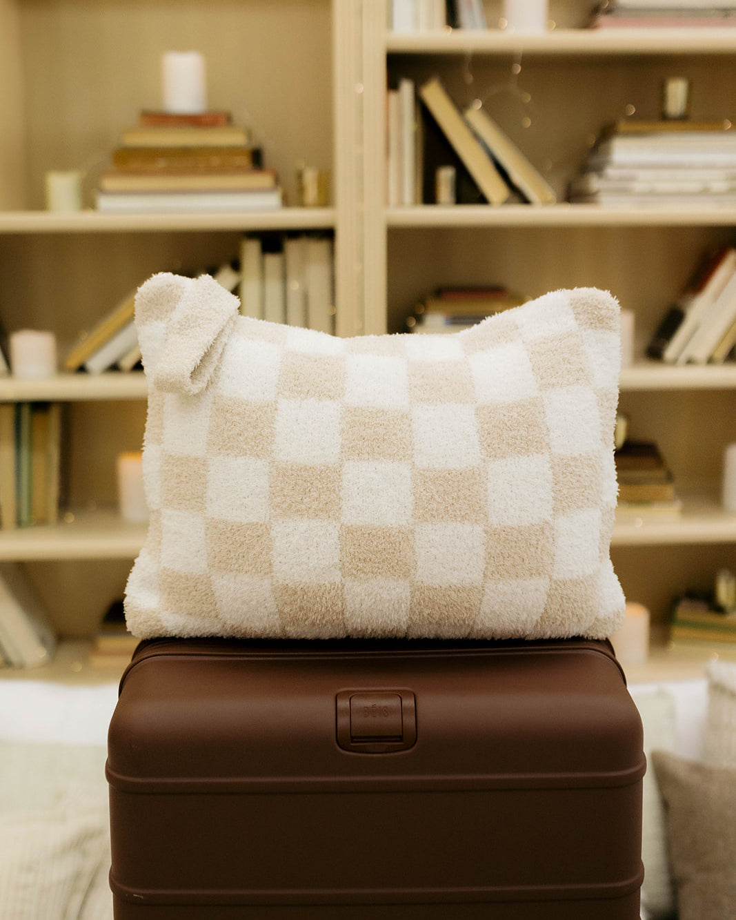 Checkered pillow on a brown suitcase with a bookshelf in the background