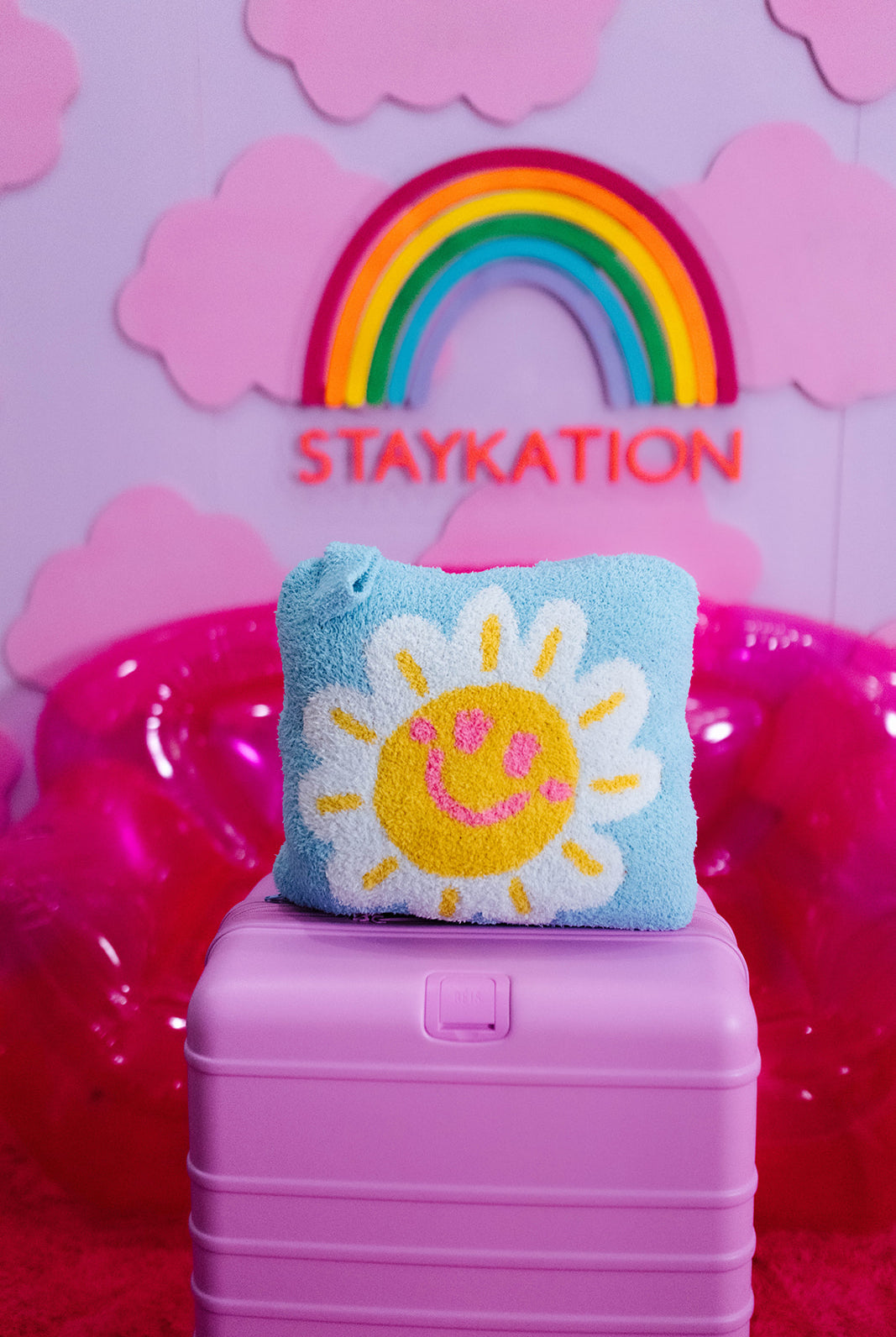 Blue quillow with a sun design on a pink suitcase against a colorful background with 'STAYKATION' text.