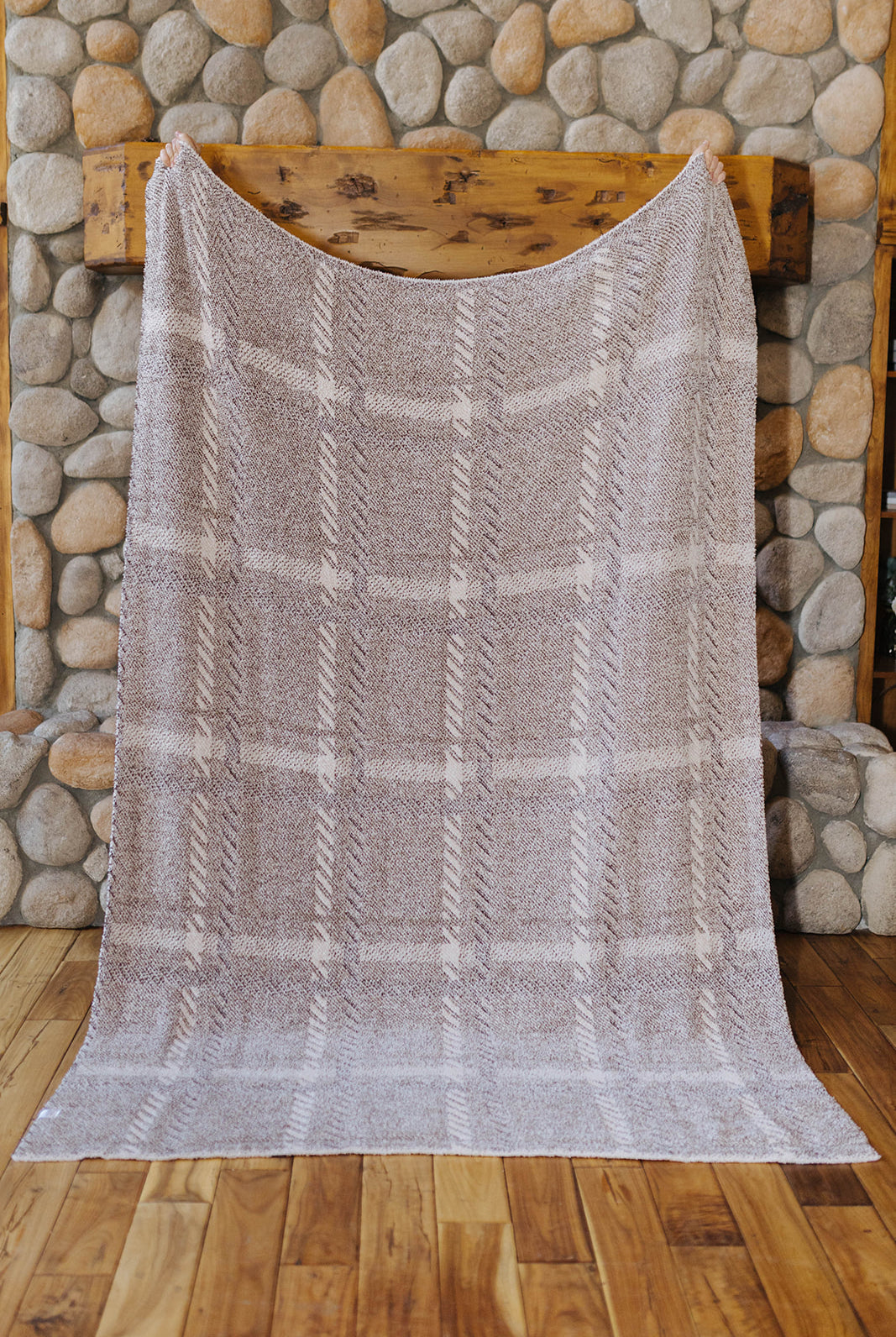 Reverse of the plaid blanket held open by a stone fireplace.