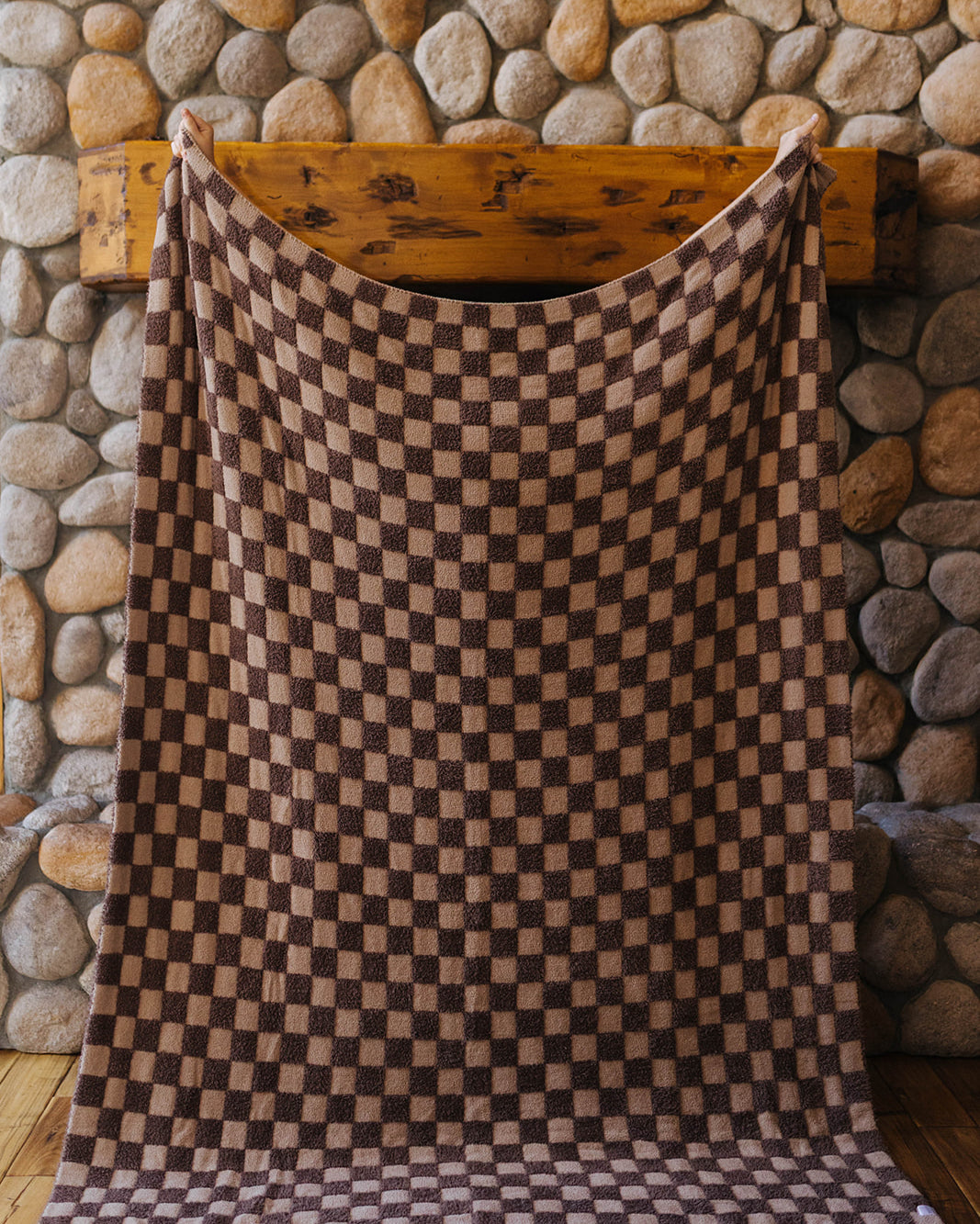 Brown check blanket held open at full size in front of a stone fireplace.