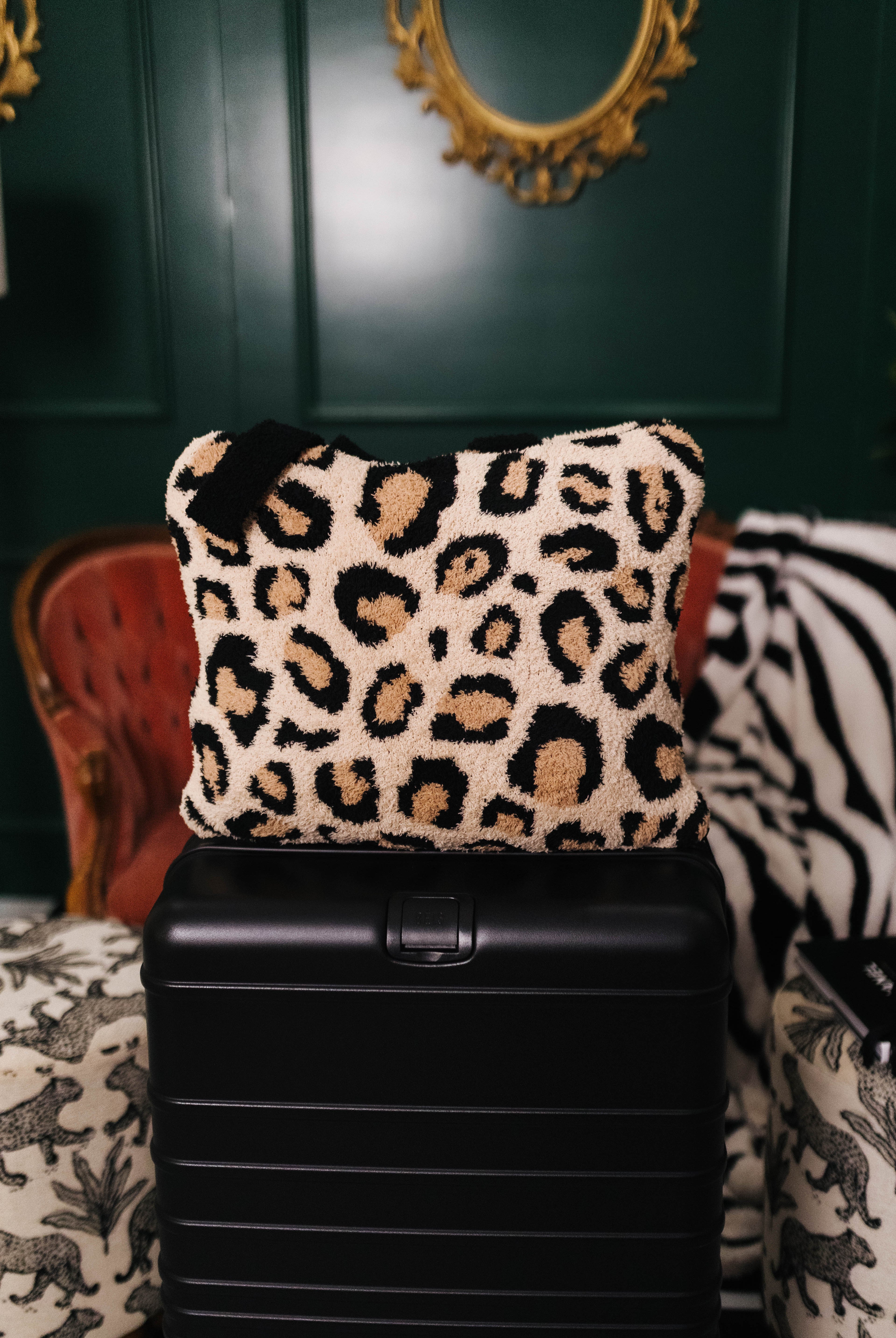 Leopard print quillow on a black suitcase with a decorative background