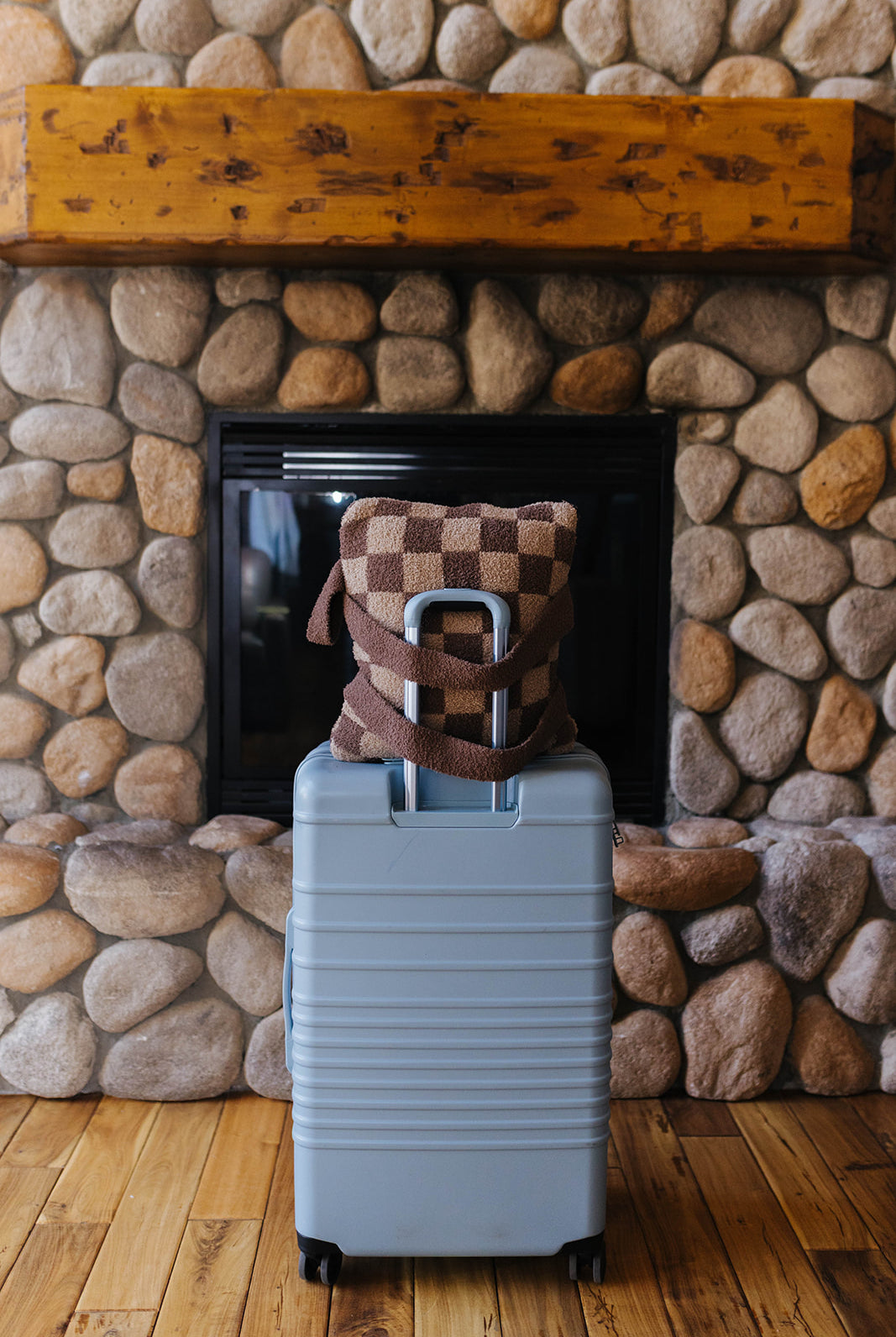 Brown check quillow displayed with its backpack straps on a suitcase.