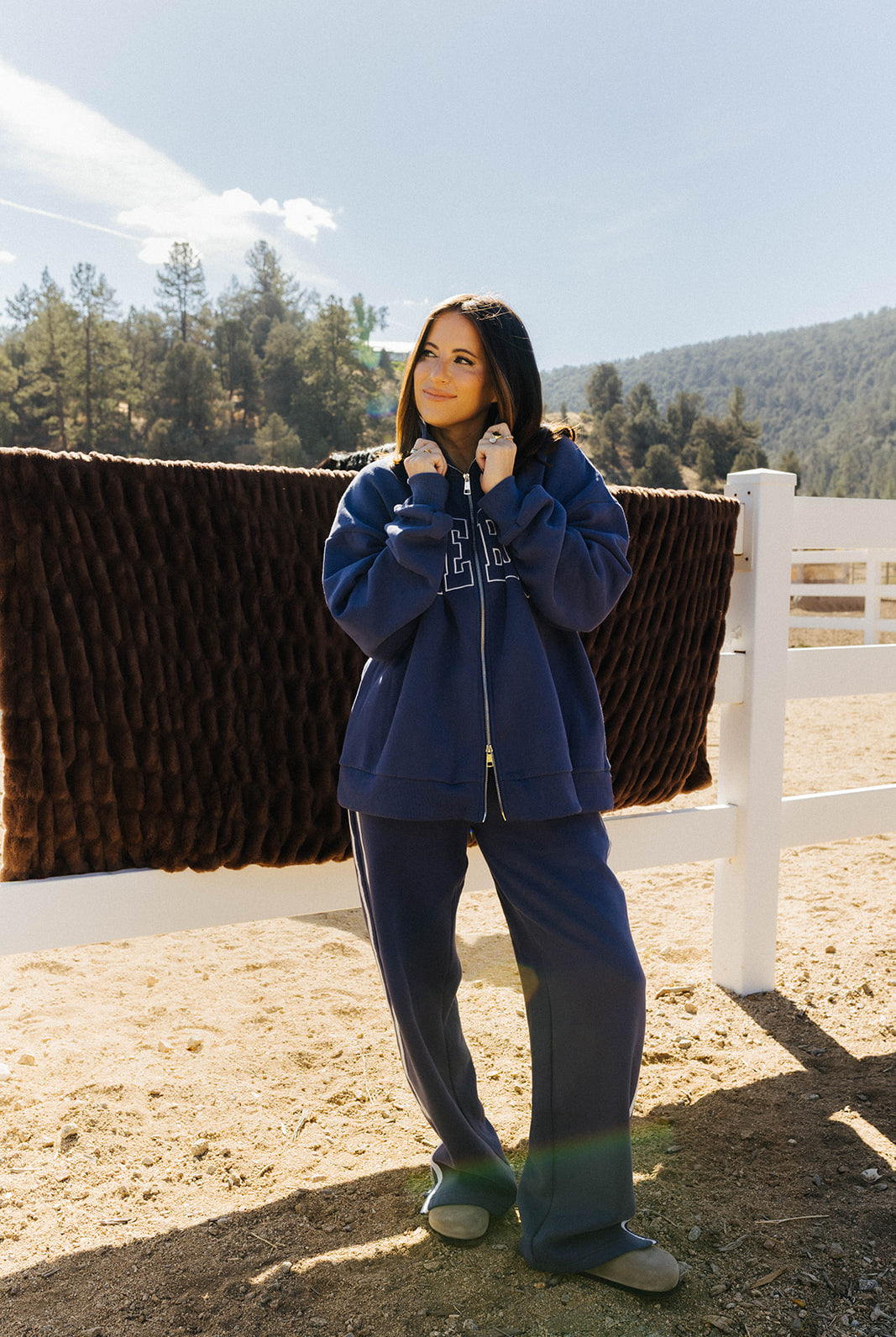 Model in a navy Homebody zip sweatshirt and matching pants beside a chocolate brown faux fur blanket on a fence.