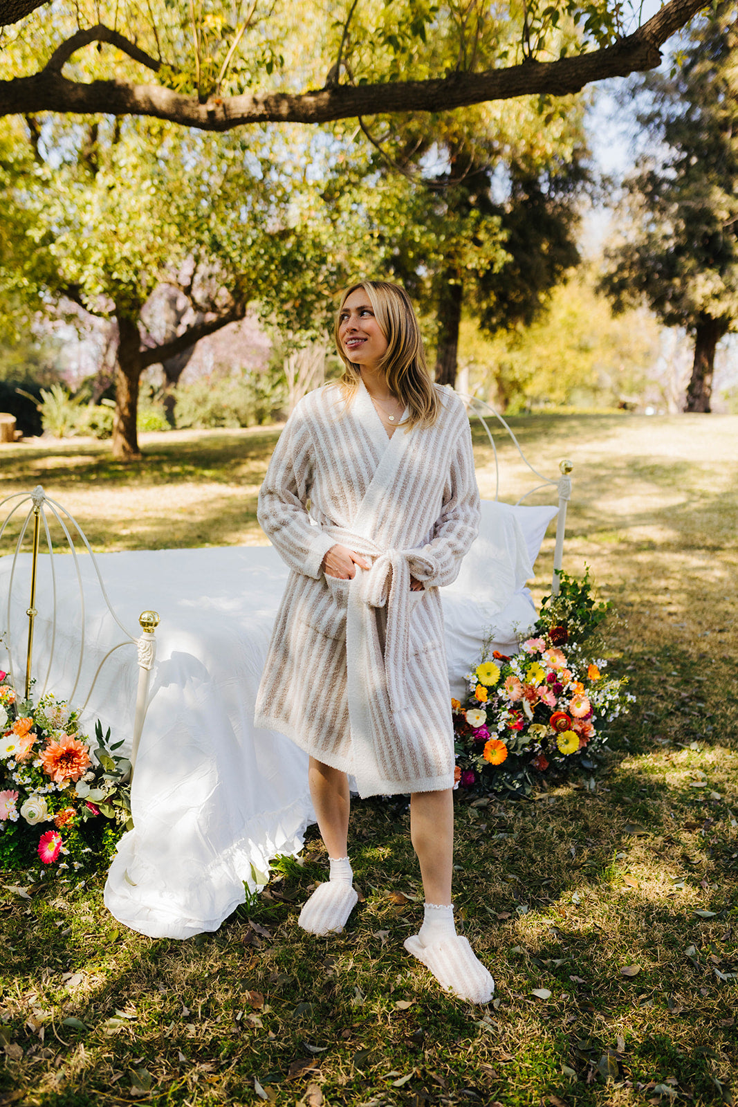 Woman in a striped robe standing outdoors with flowers and a canopy in the background