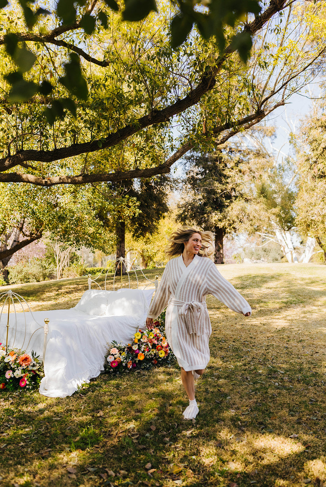 Woman in a robe standing outdoors with a decorated arch and flowers in the background