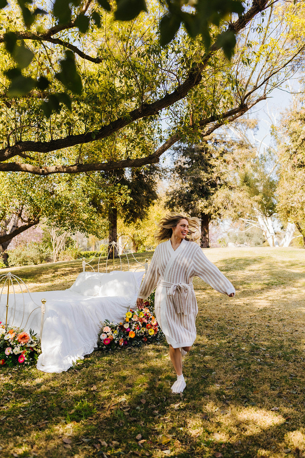 Woman in a robe standing outdoors with a decorated arch and flowers in the background