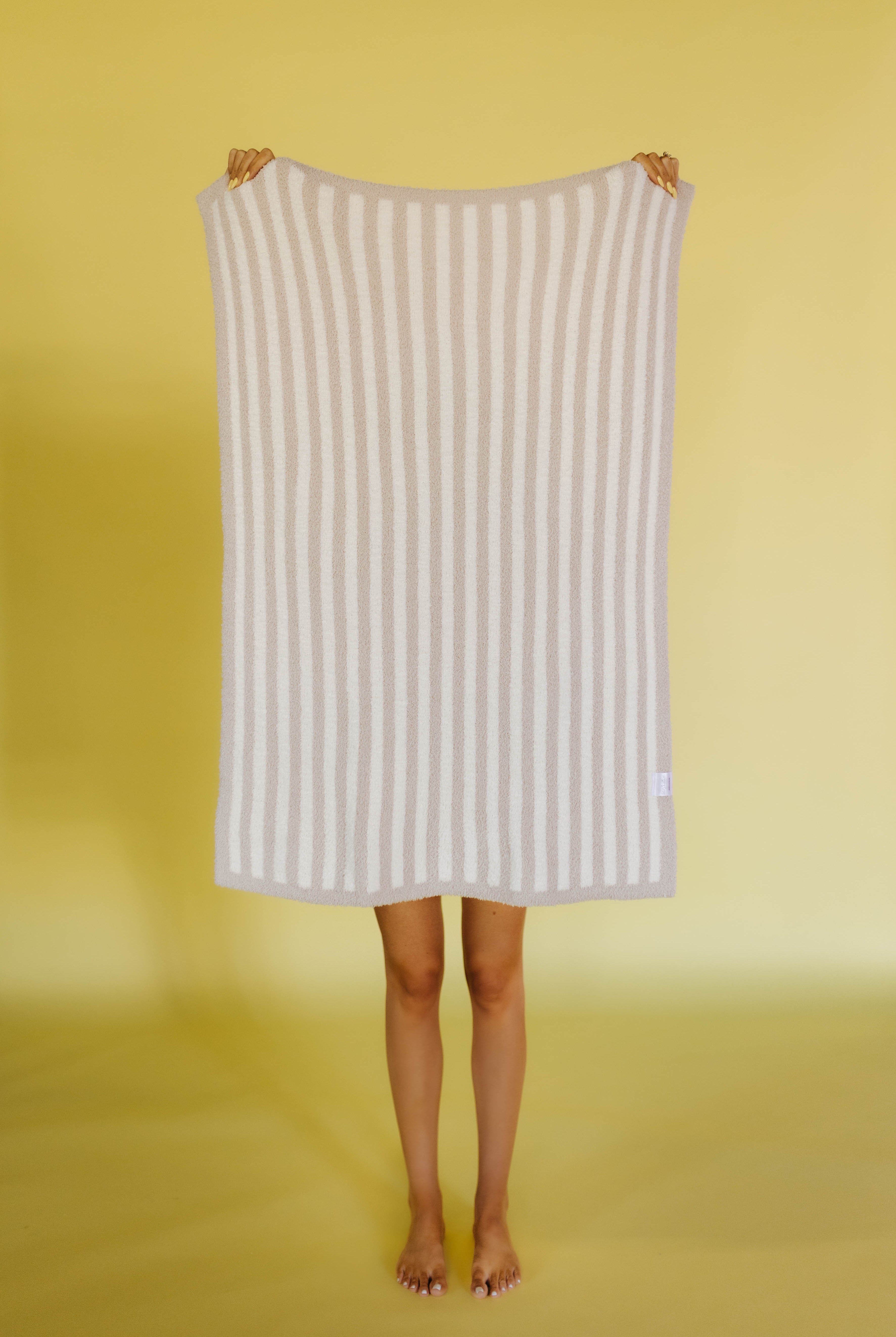 Person holding a white and beige striped kid blanket against a yellow background