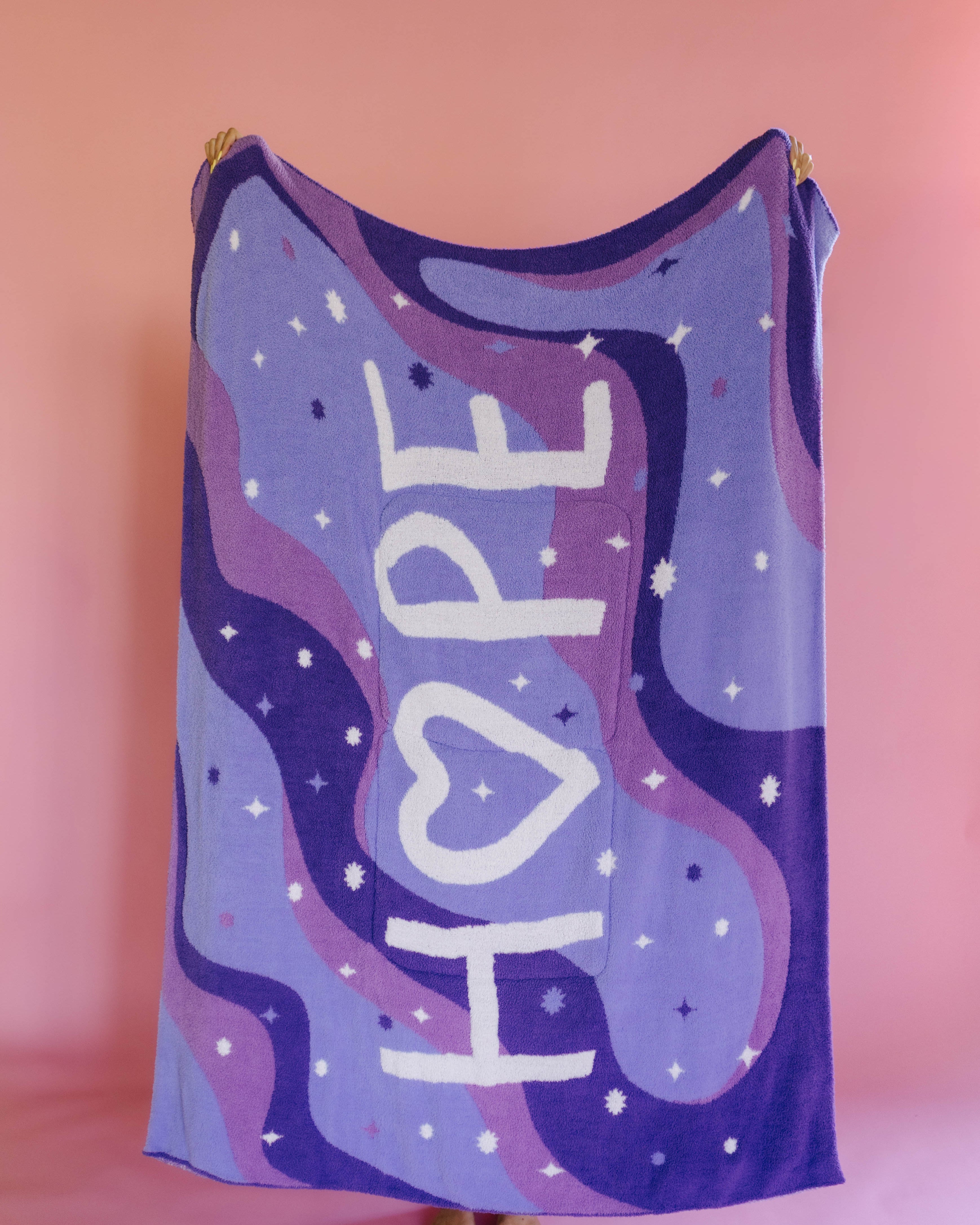A person holding up the full size quillow with white stars, and the word 'HOPE' in large white letters, standing against a pink background.