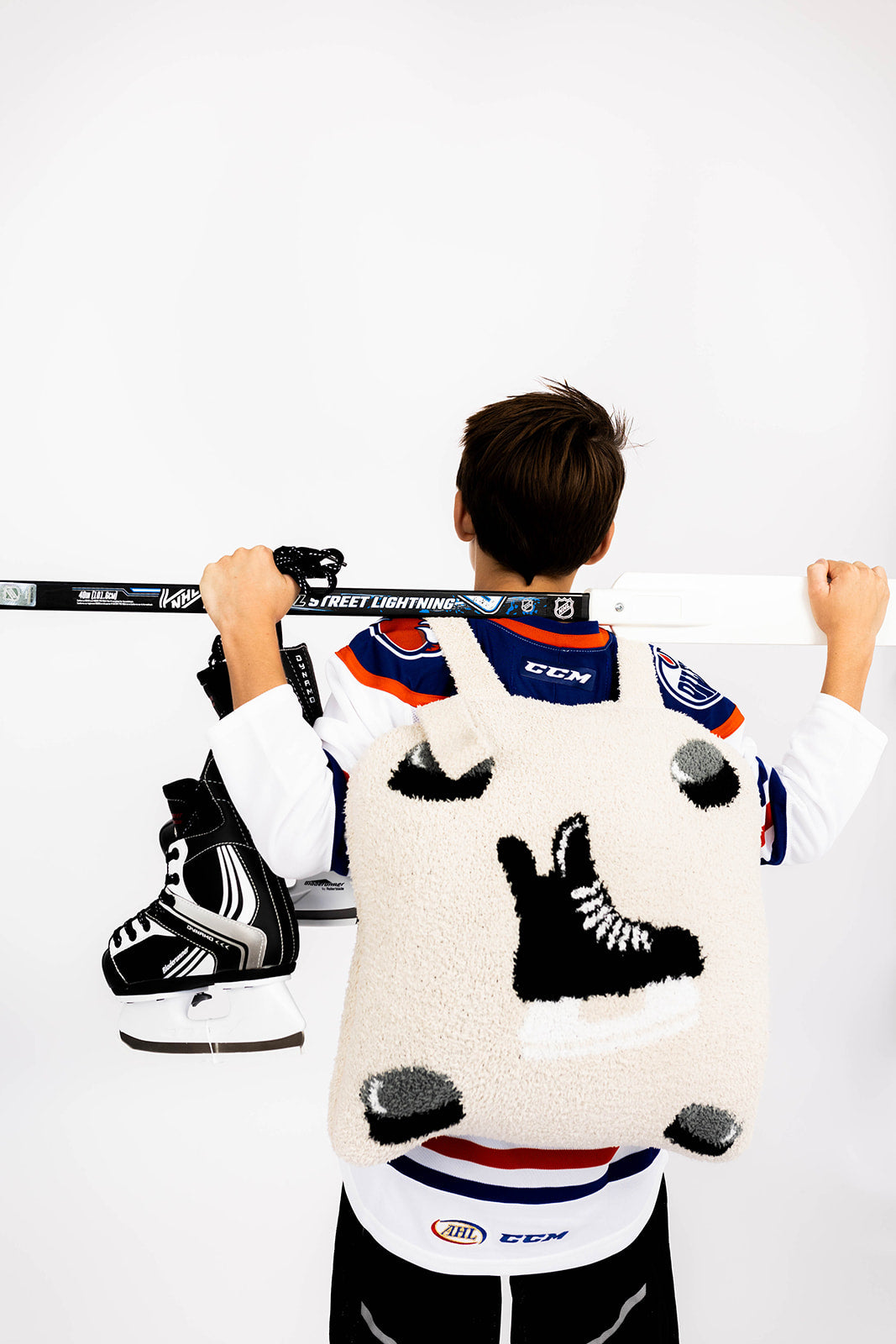 Person wearing a hockey jersey with a unique design and wearing hockey quillow, holding a hockey stick on a white background
