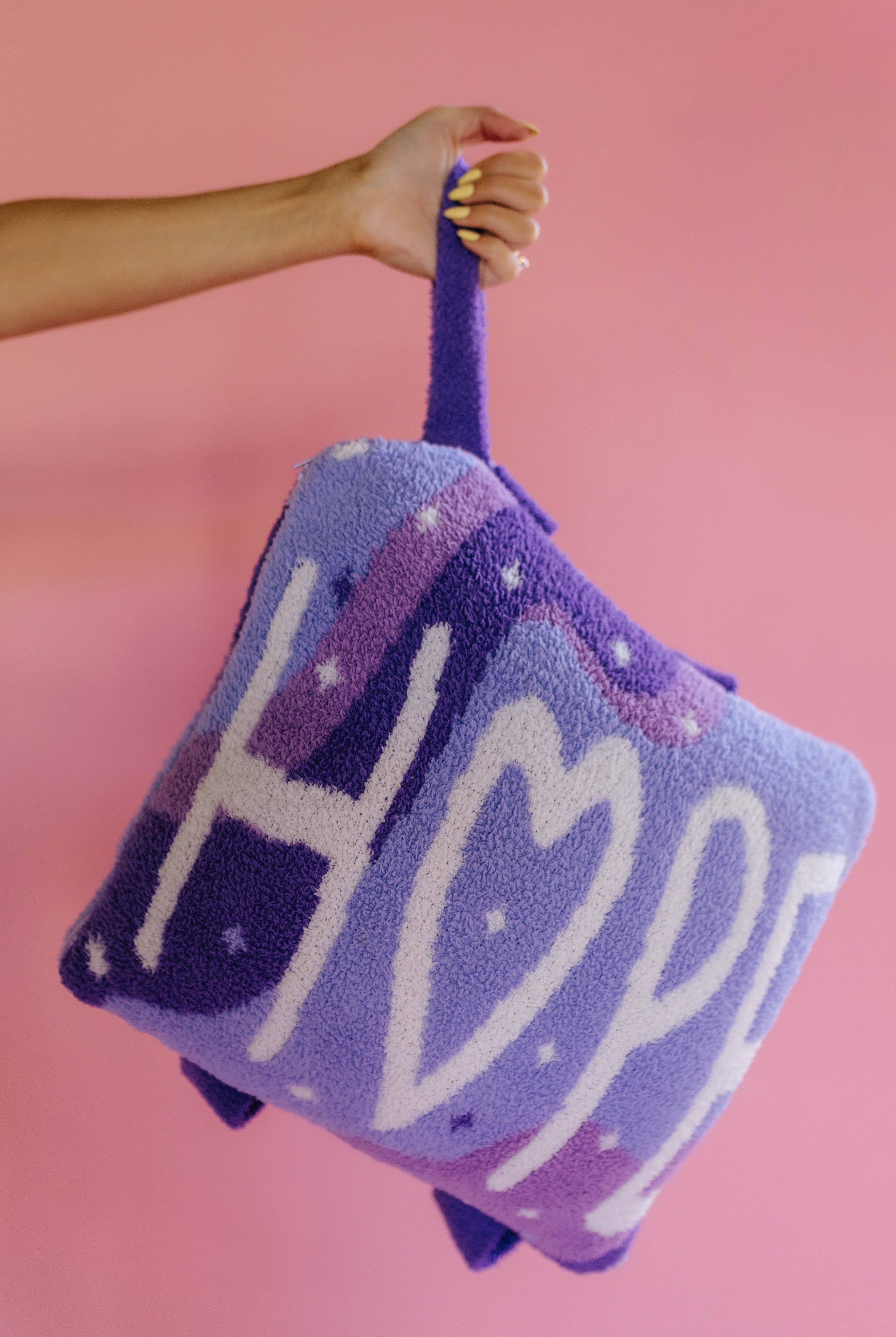 holding the quillow by the wristlet strap on a solid back background