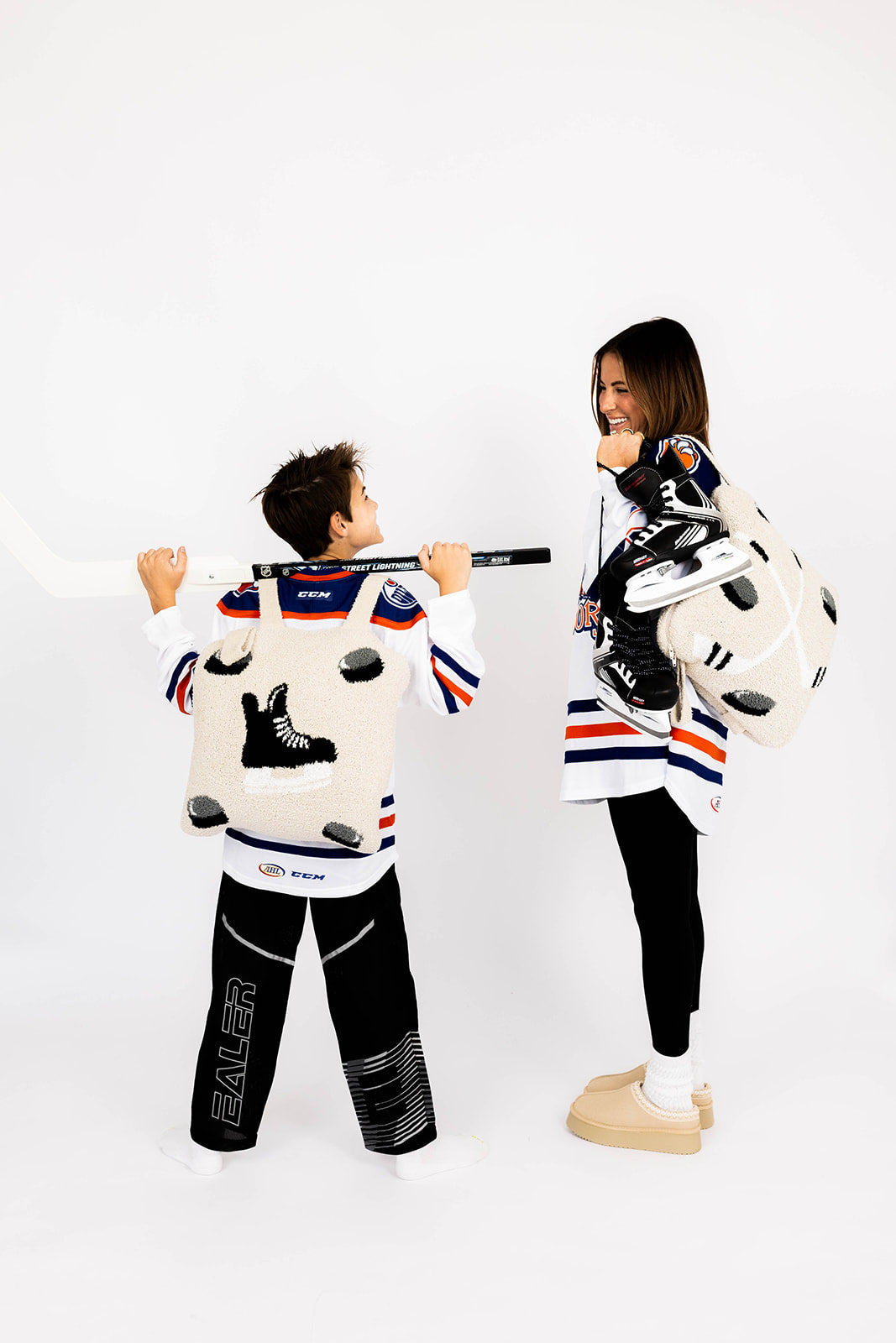 Two people wearing matching hockey-themed outfits with hockey skates and stick, both wearing hockey quillows on a white background