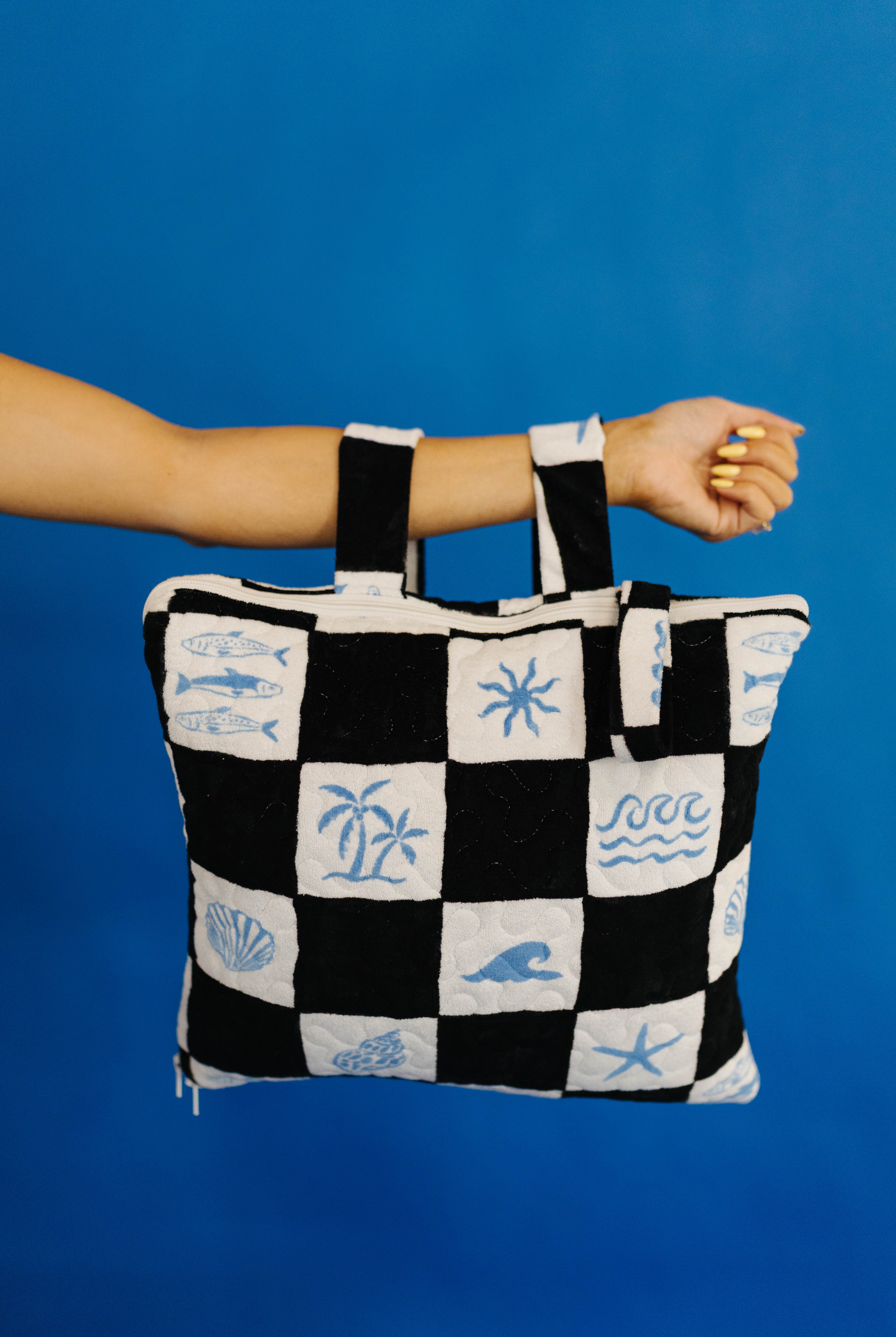 Black and white checkered picnic quillow with beach-themed patterns held against a blue background