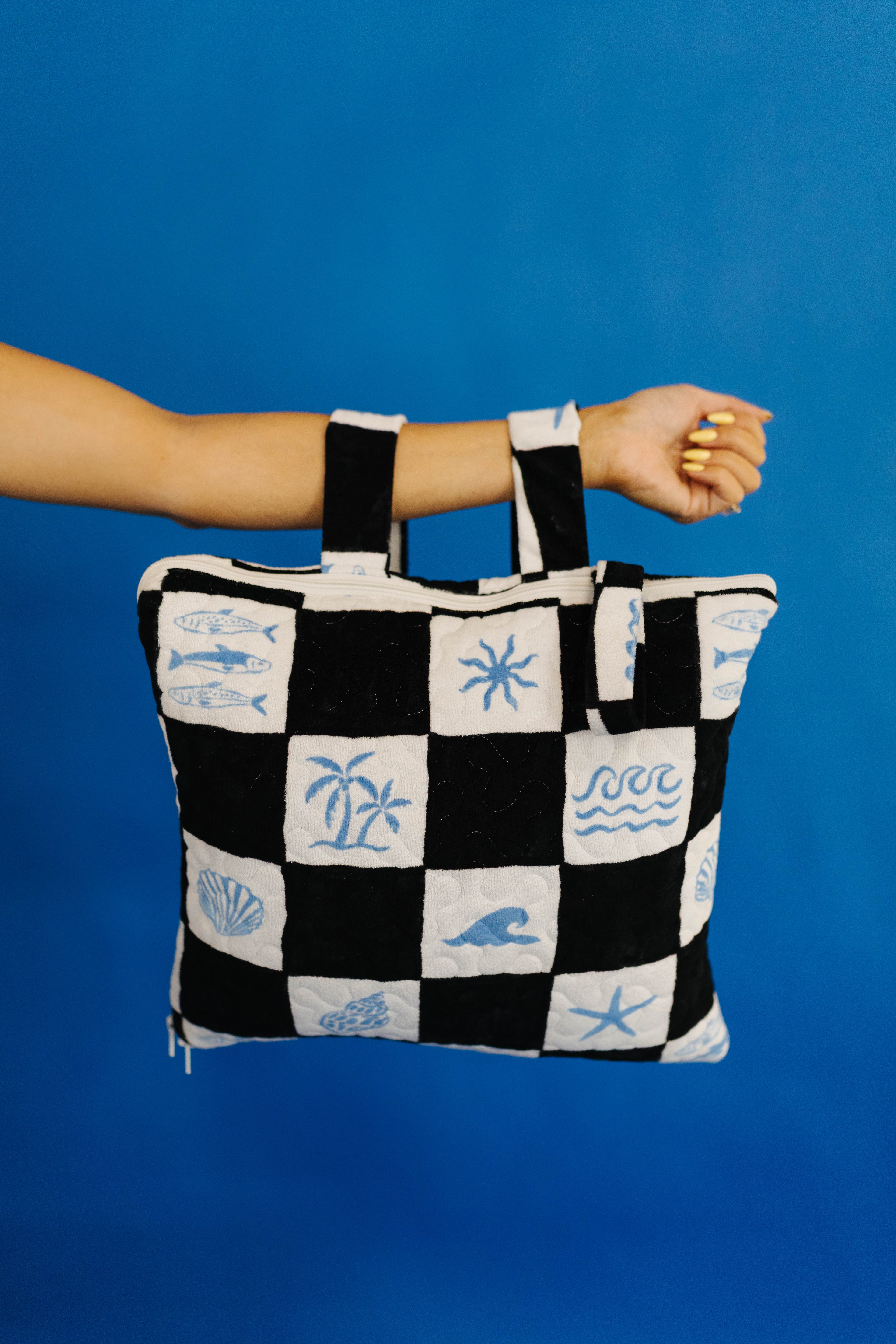 Black and white checkered picnic quillow with beach-themed patterns held against a blue background