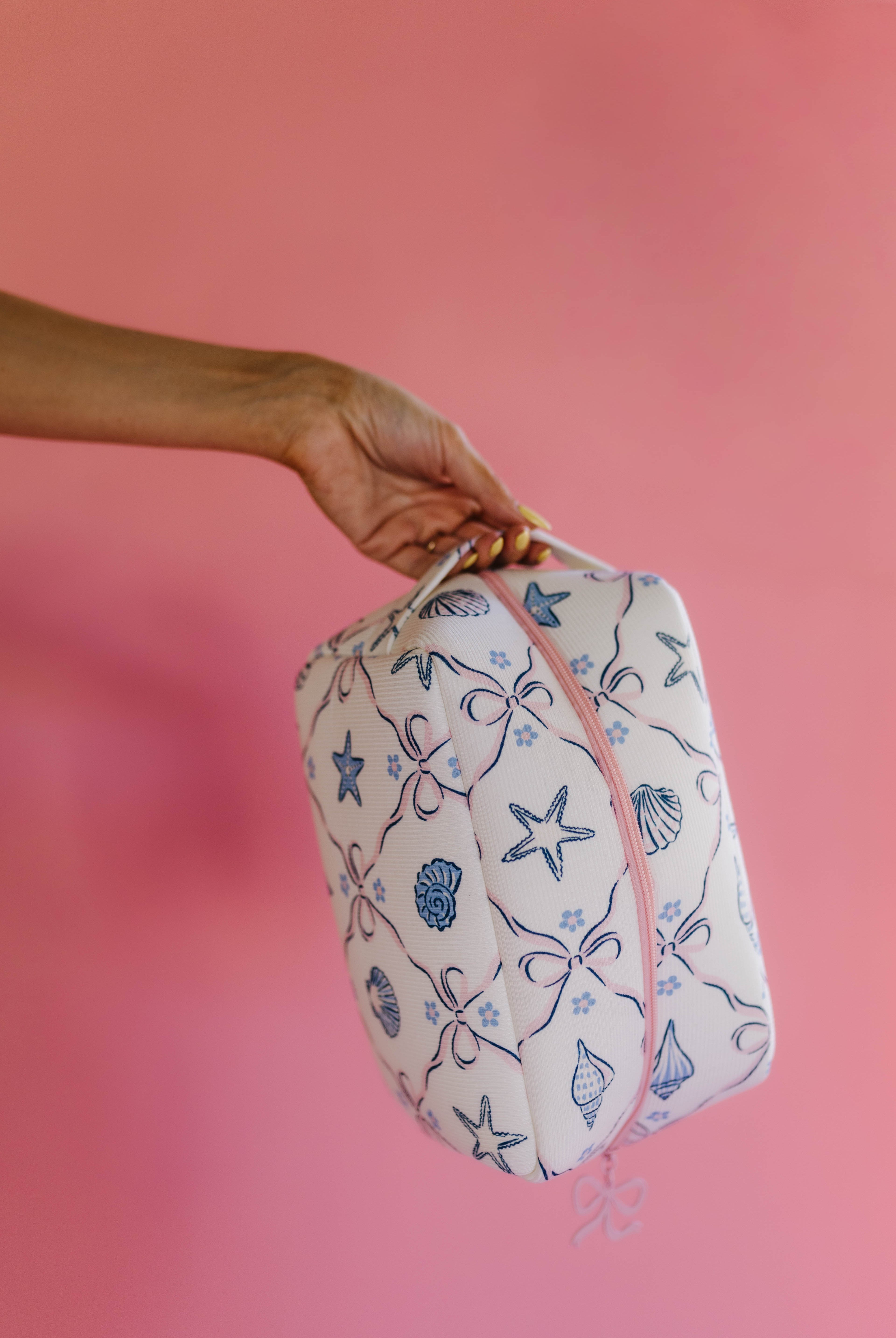 Hand holding a patterned bag against a pink background