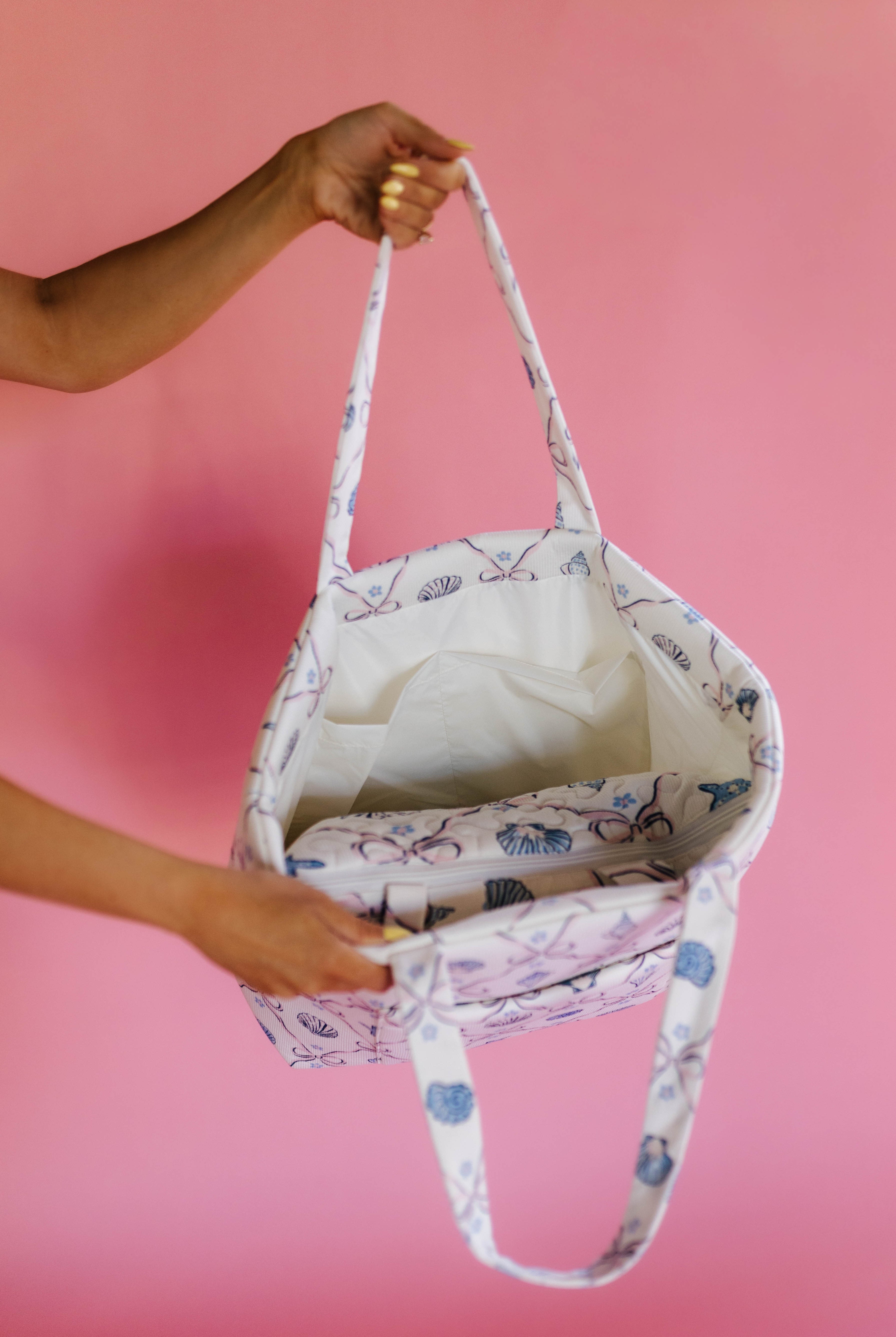 Person holding a beach- patterned bag against a pink background