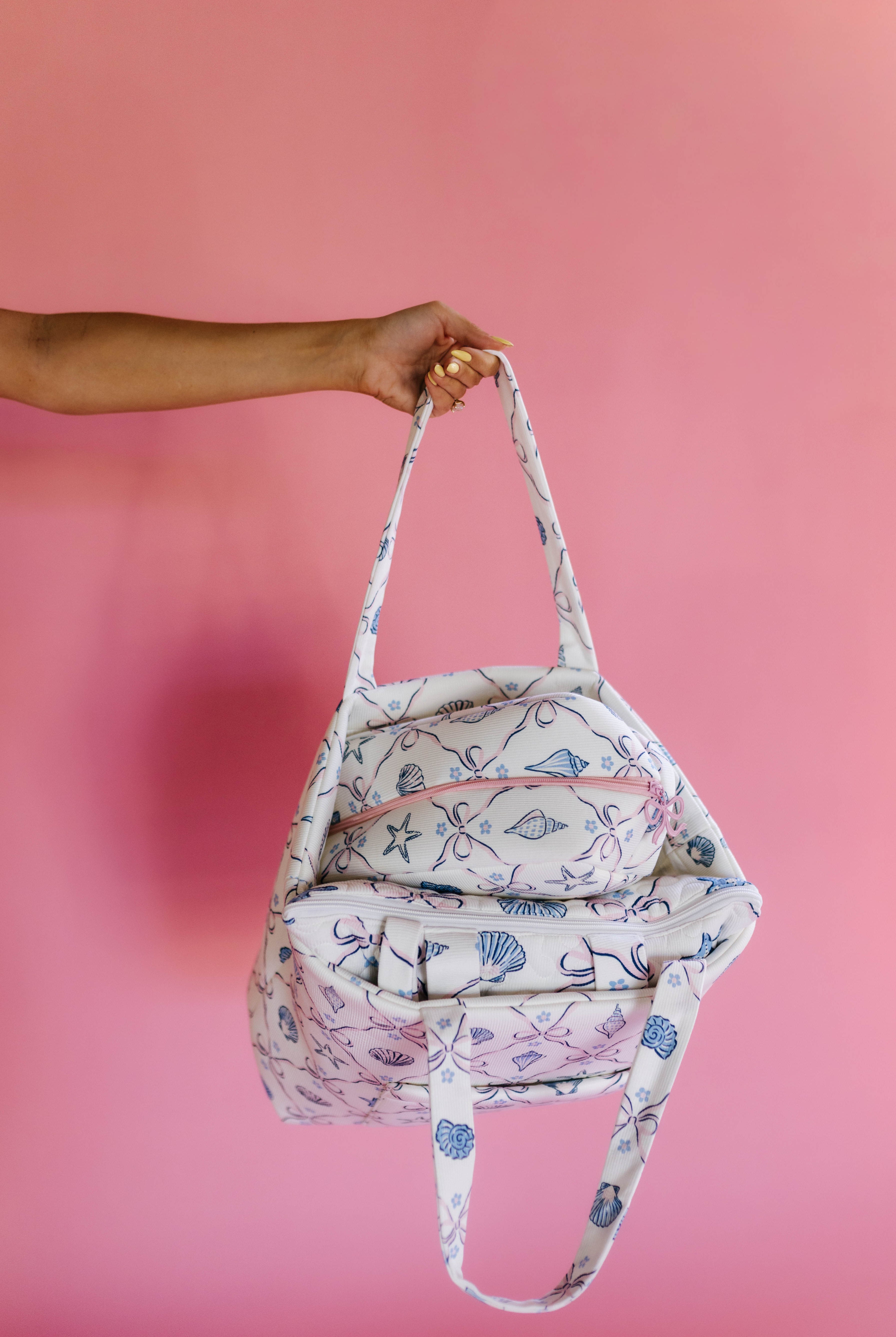 Person holding a patterned bag against a pink background