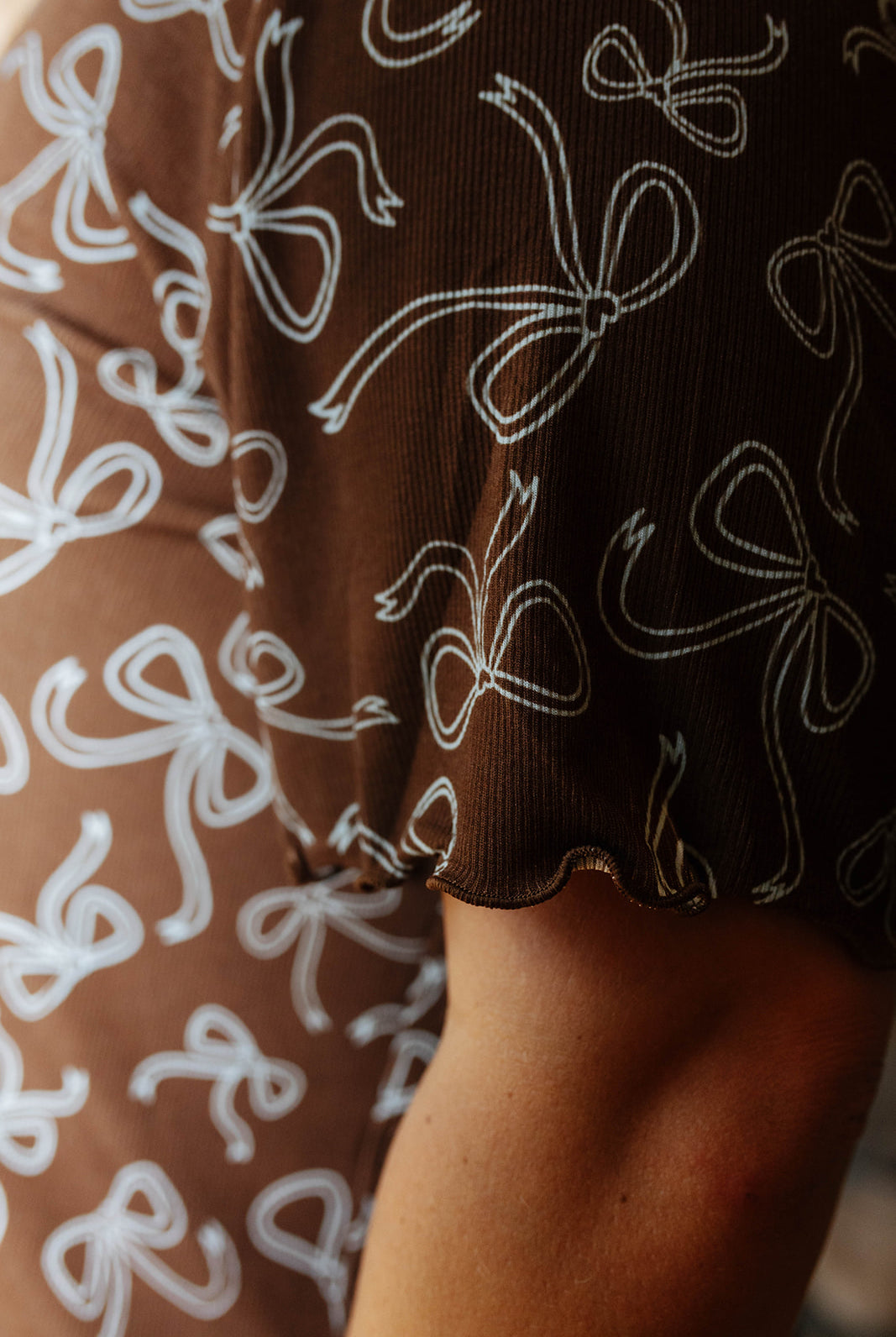 Close view of the scalloped sleeve edge on the brown bow print pajama top.