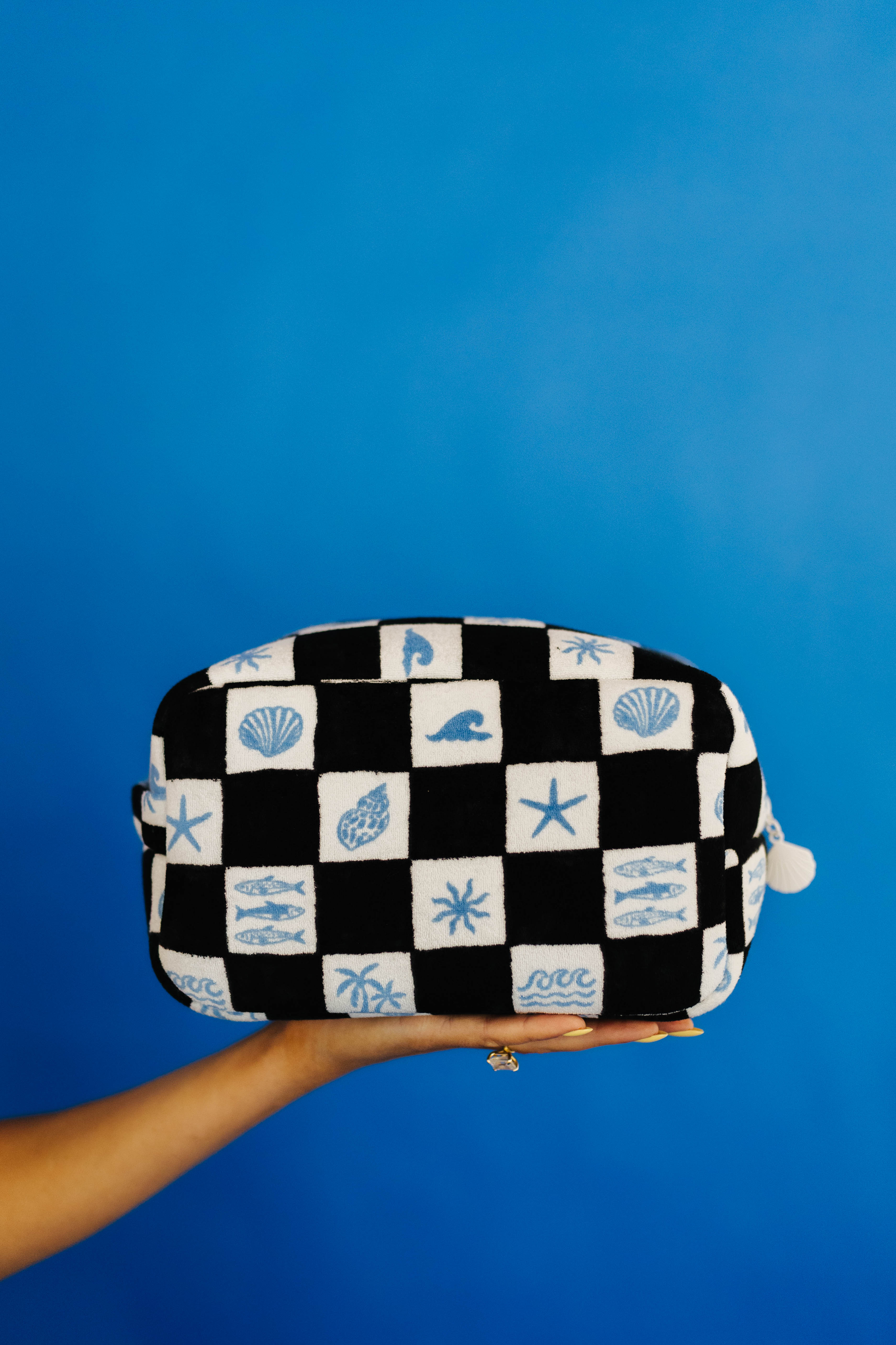 Checkered cosmetic bag with sea-themed patterns held against a blue background