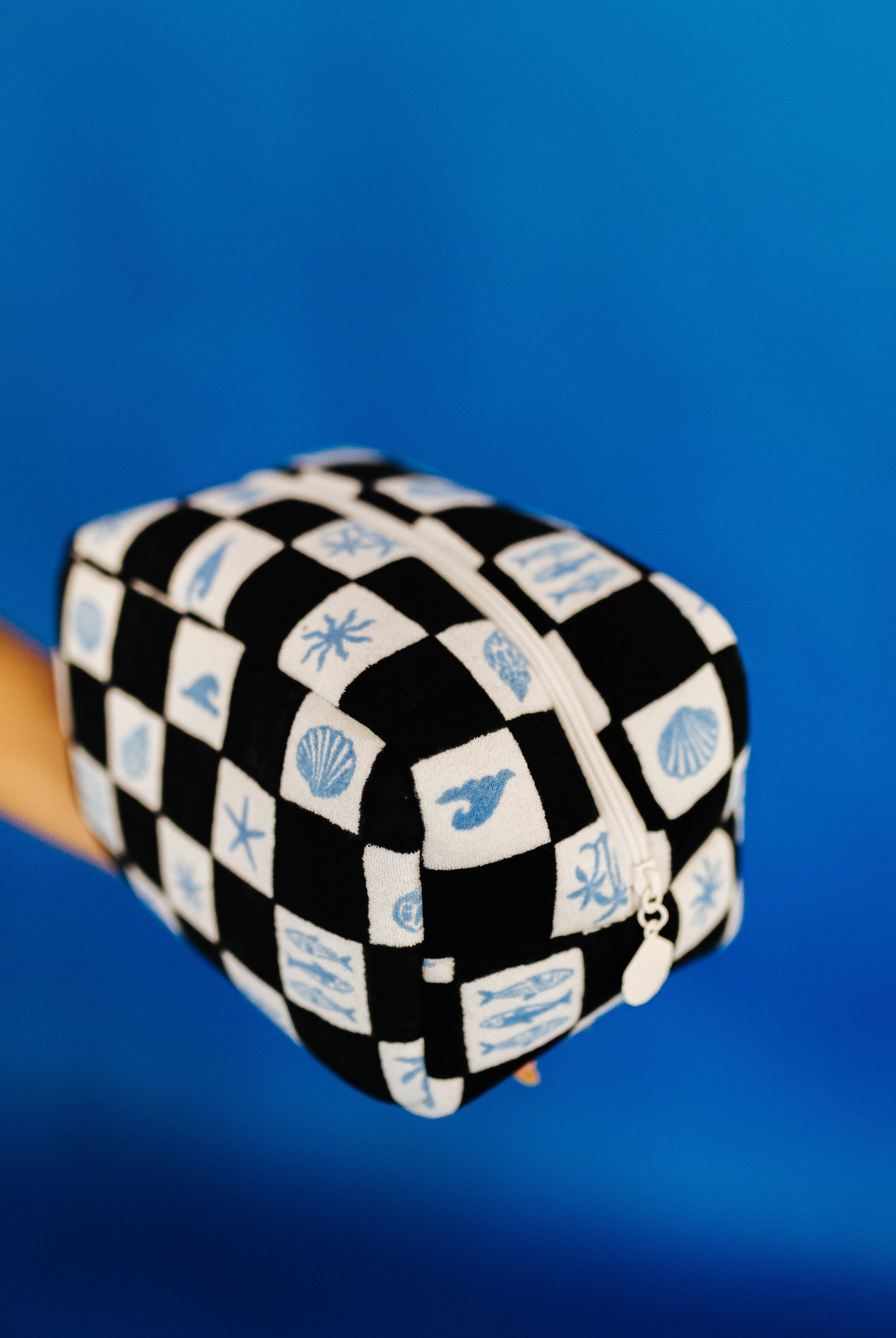 Black and white checkered cosmetic bag with blue sea-themed designs on a blue background