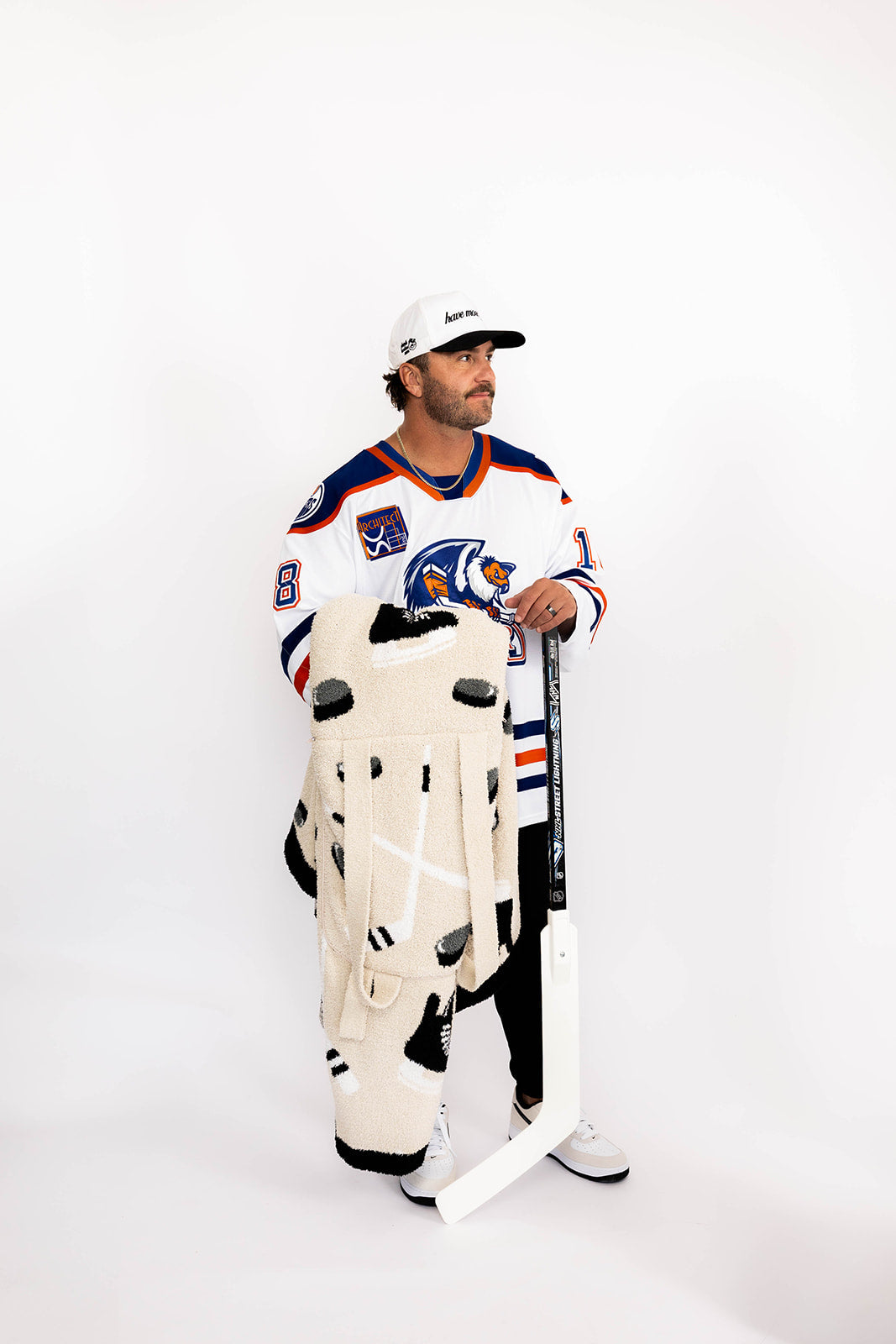 Person wearing a hockey jersey and holding a hockey stick and hockey blanket on a white background