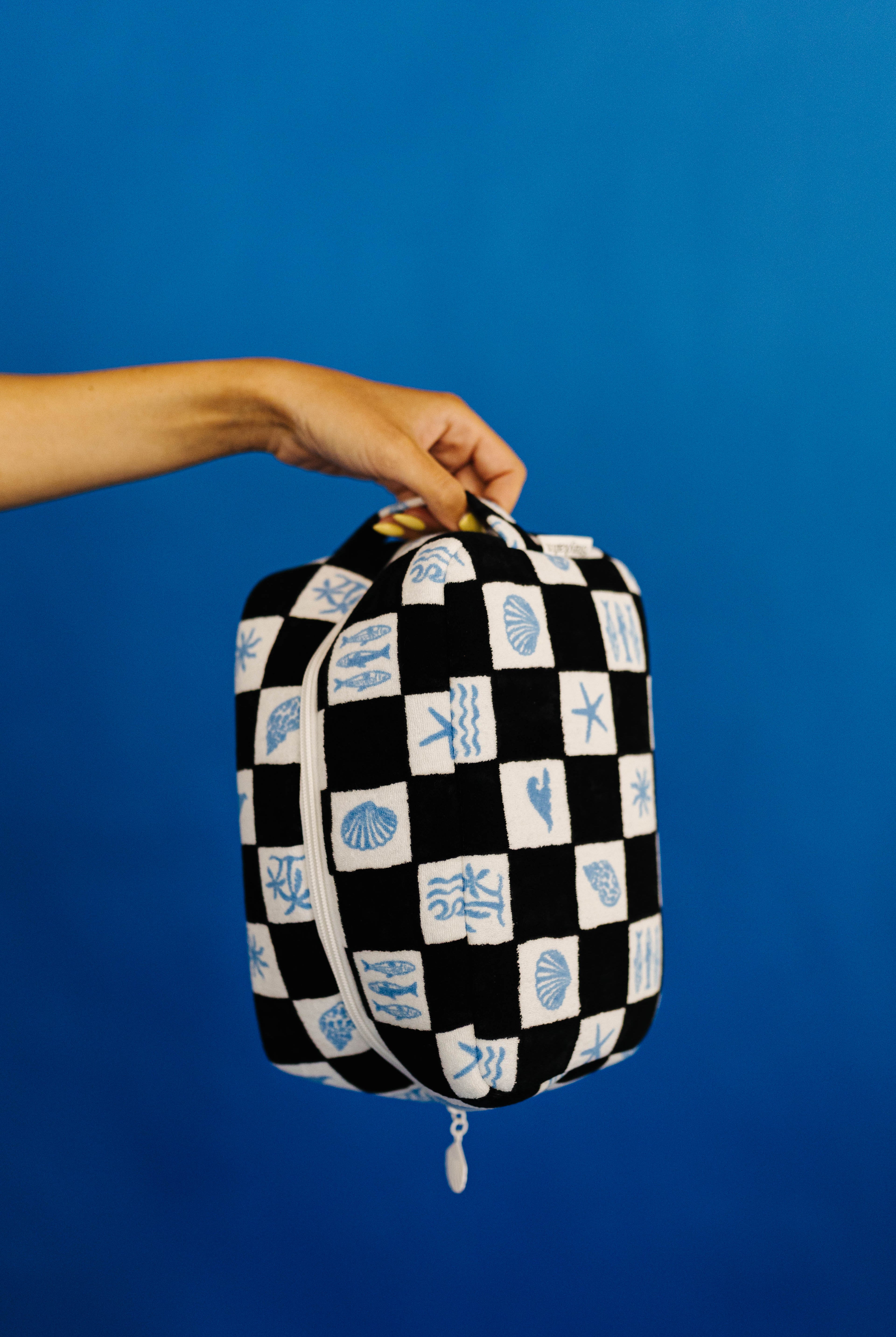 Black and white checkered bag with blue patterns held by a hand against a blue background