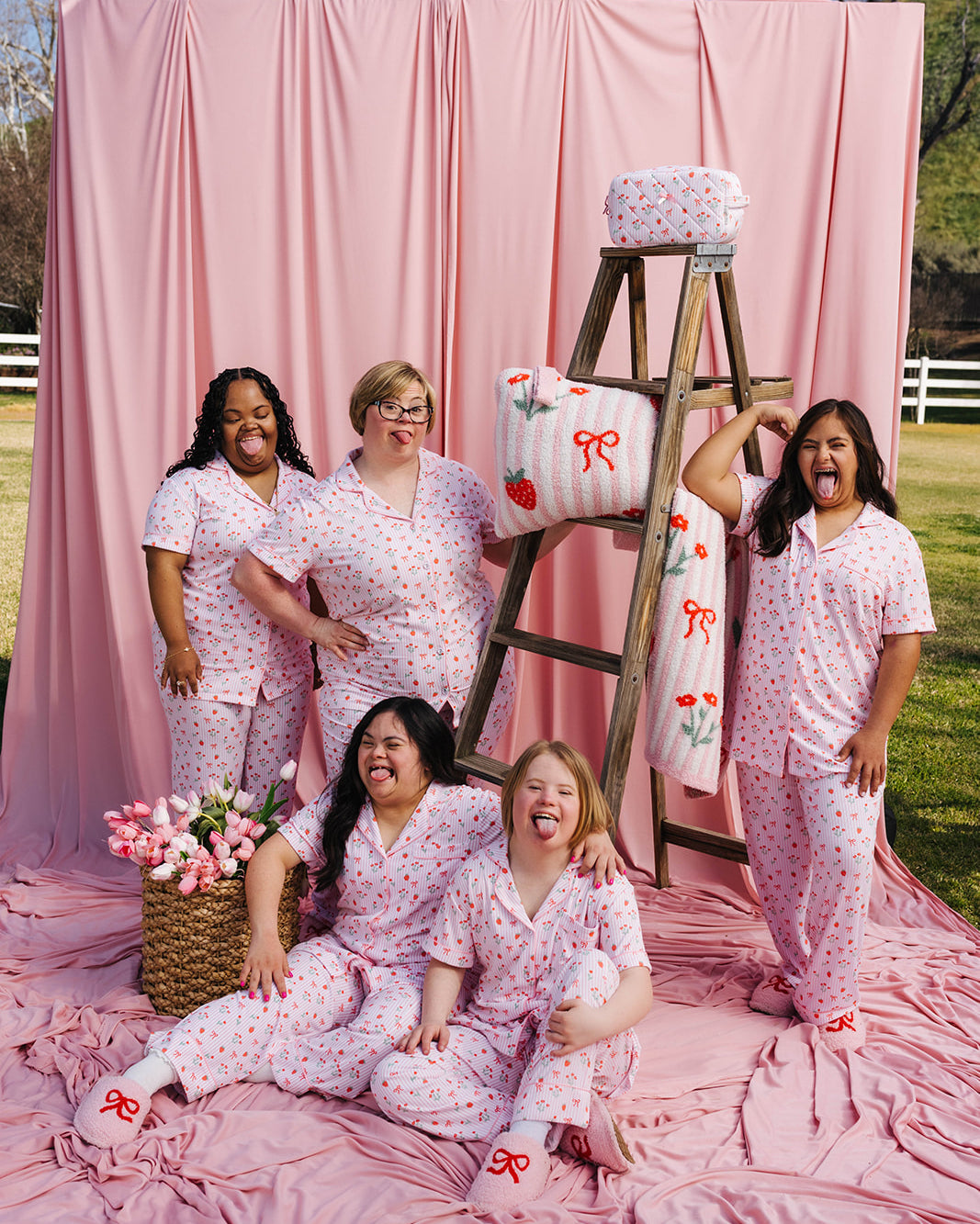 Group of people in matching pajamas posing in front of a pink backdrop with a ladder and decorative items.