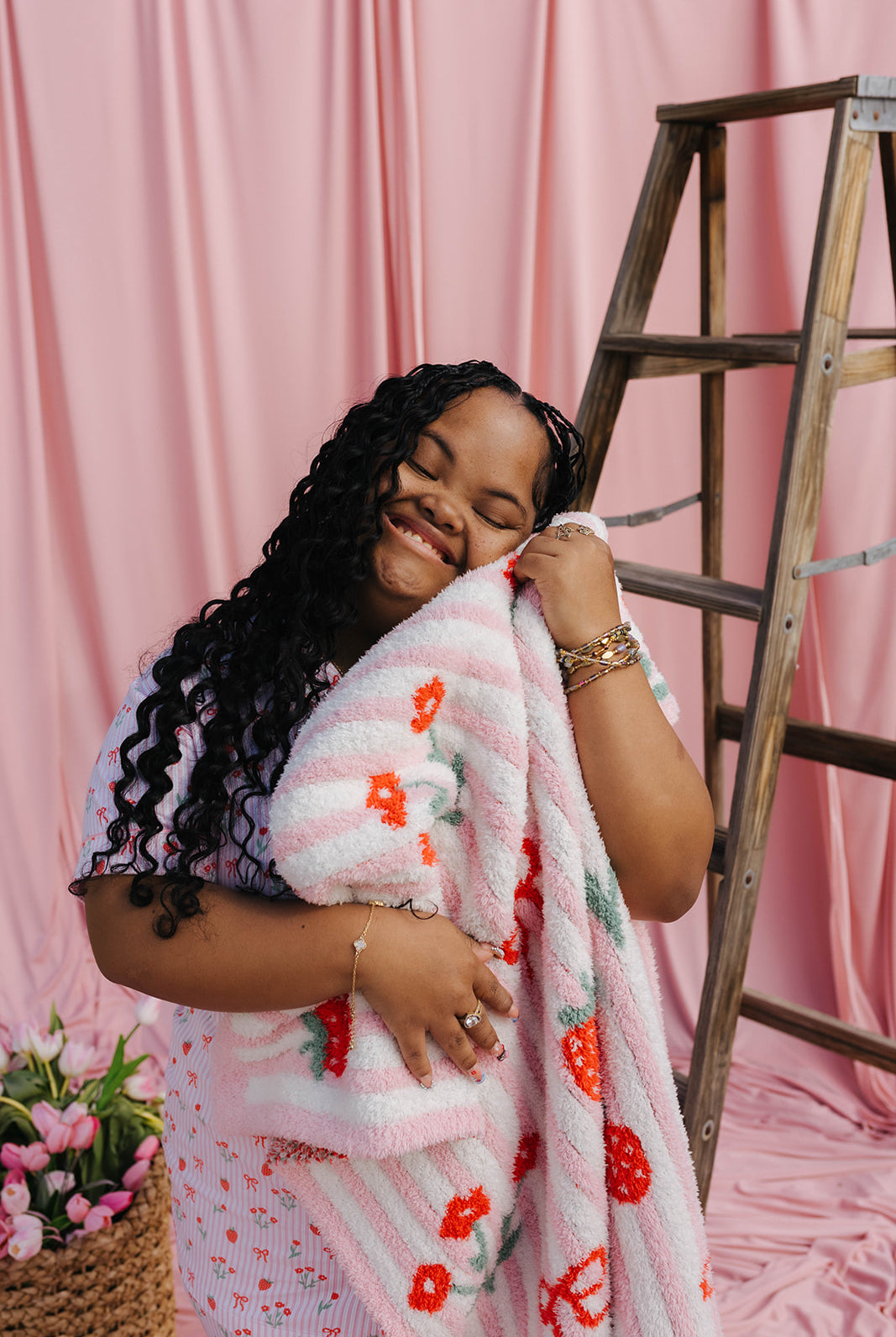 Woman wrapped in a floral blanket against a pink curtain background