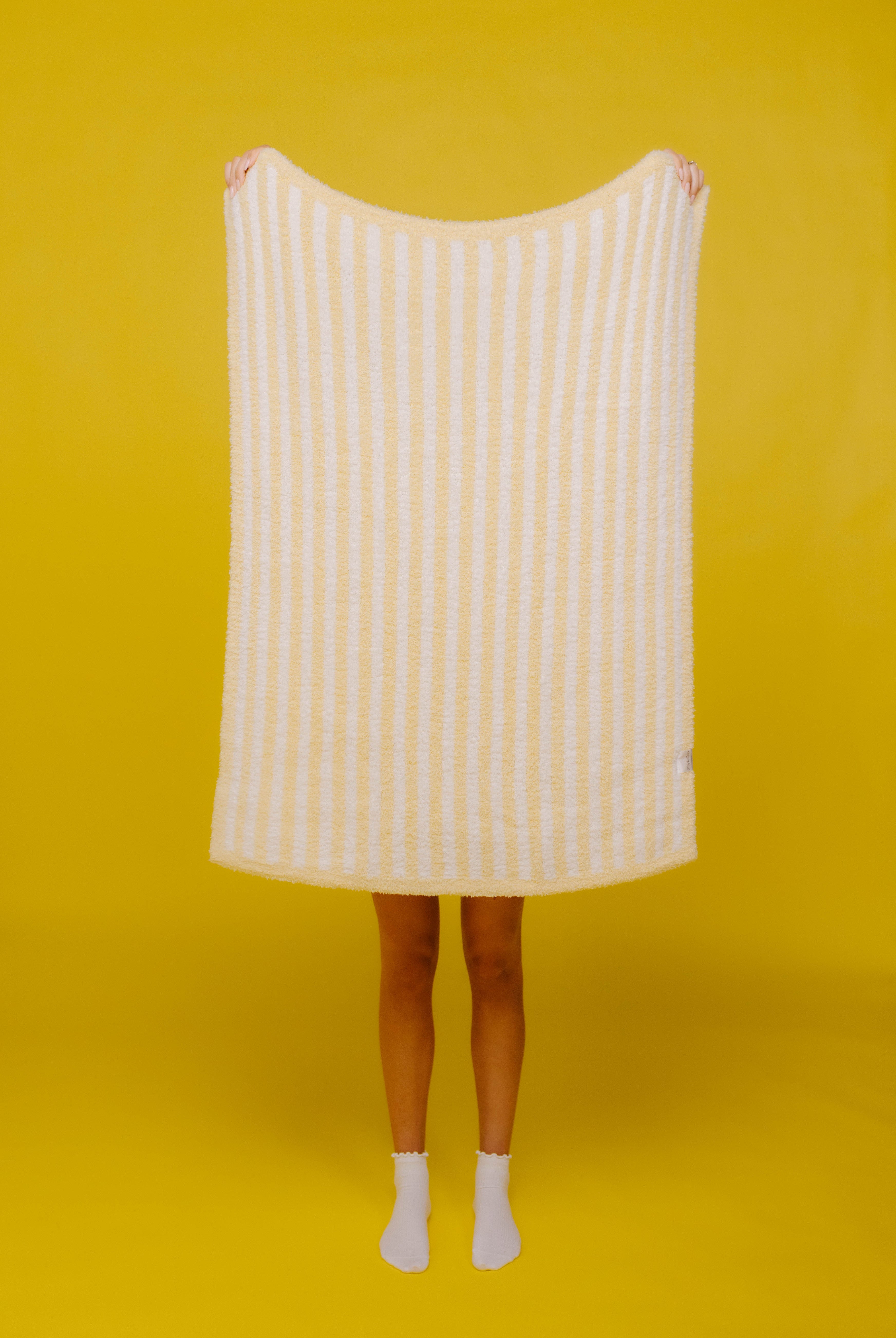 holding up butter yellow stripes baby blanket on yellow background