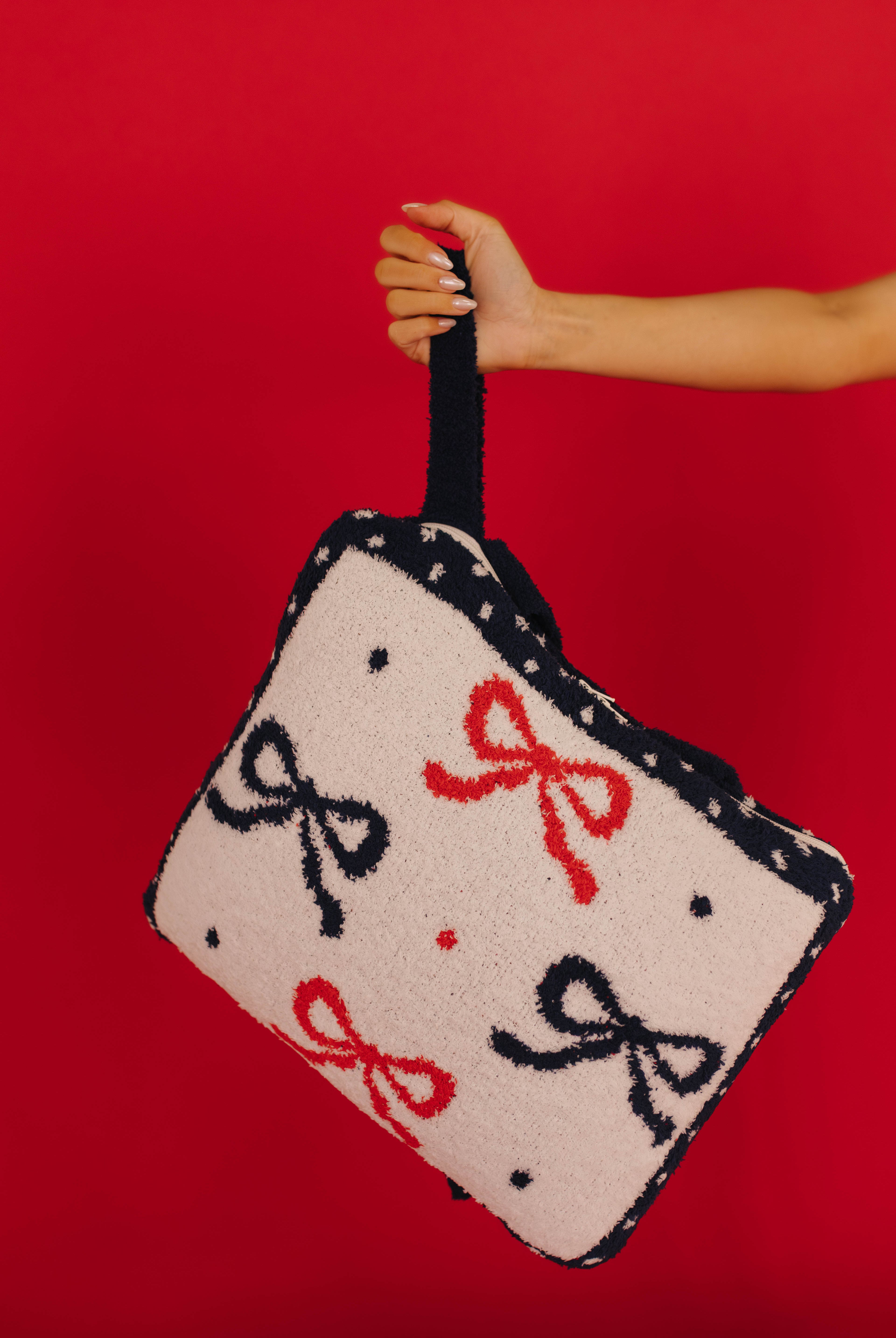 Hand holding a quillow with bow patterns against a red background