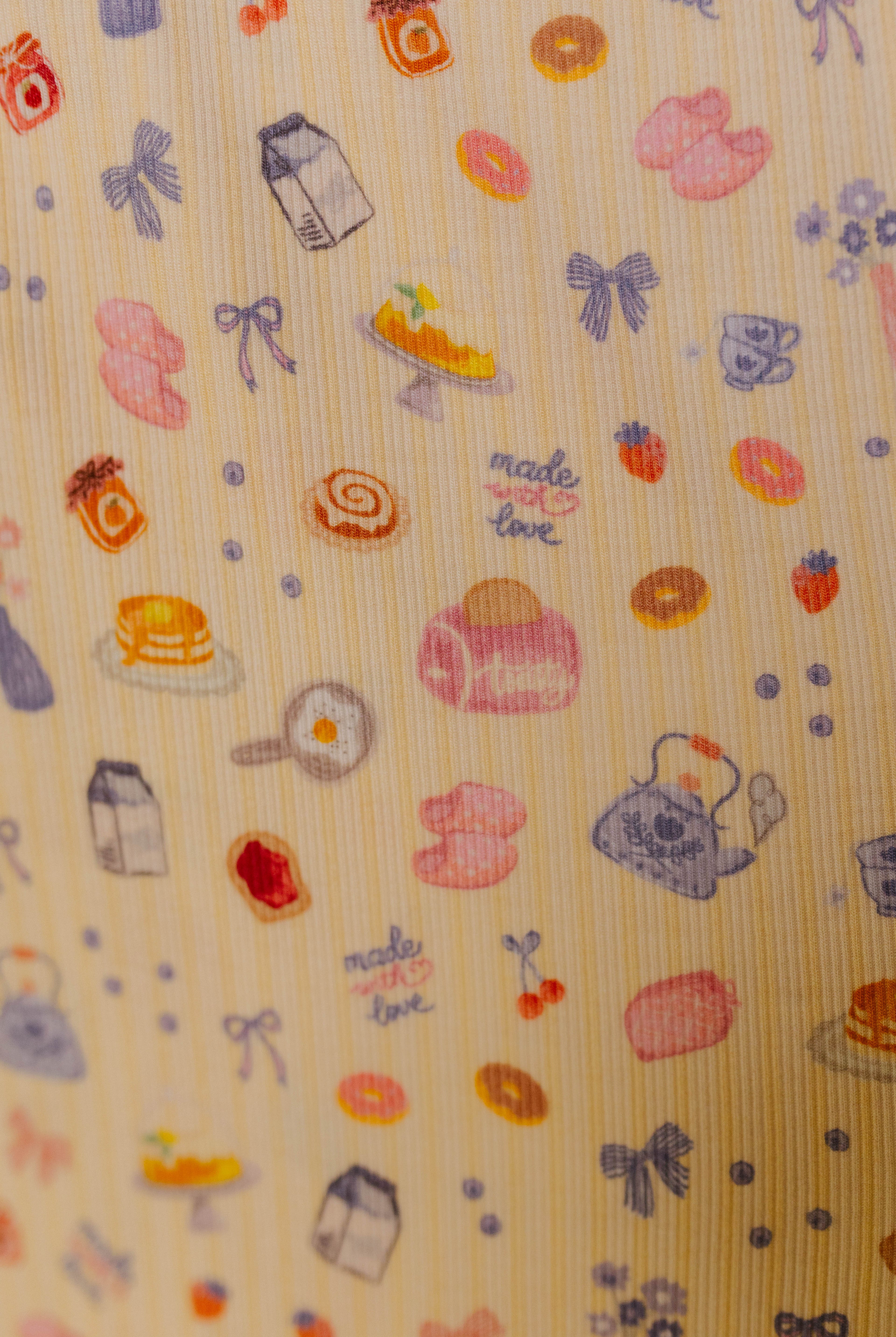 Patterned fabric with food and kitchen-themed illustrations on a butter yellow background
