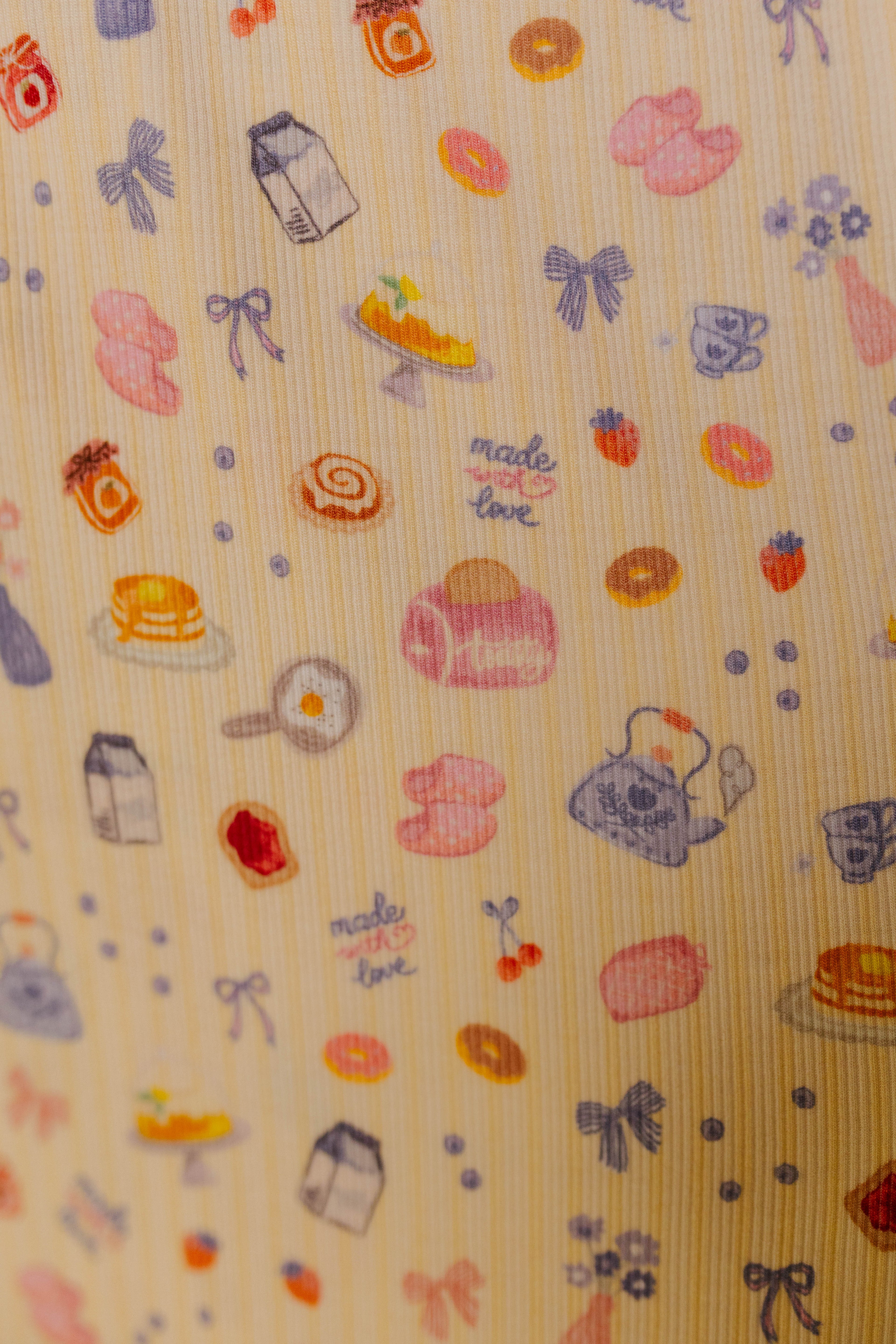 Patterned fabric with food and kitchen-themed illustrations on a butter yellow background