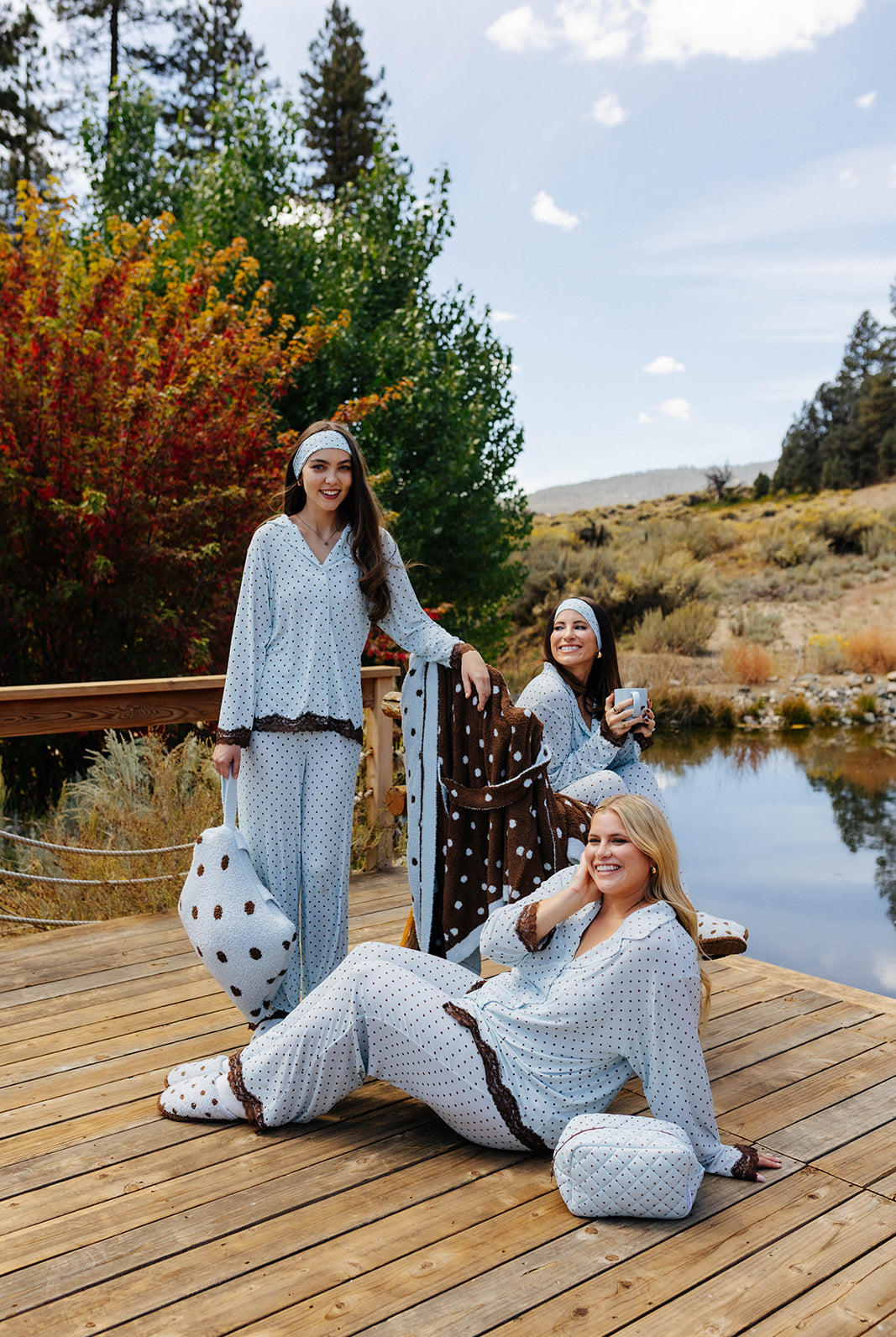 Three models in blue polka dot pajamas with brown and cream polka dot quillows on a lakeside dock.