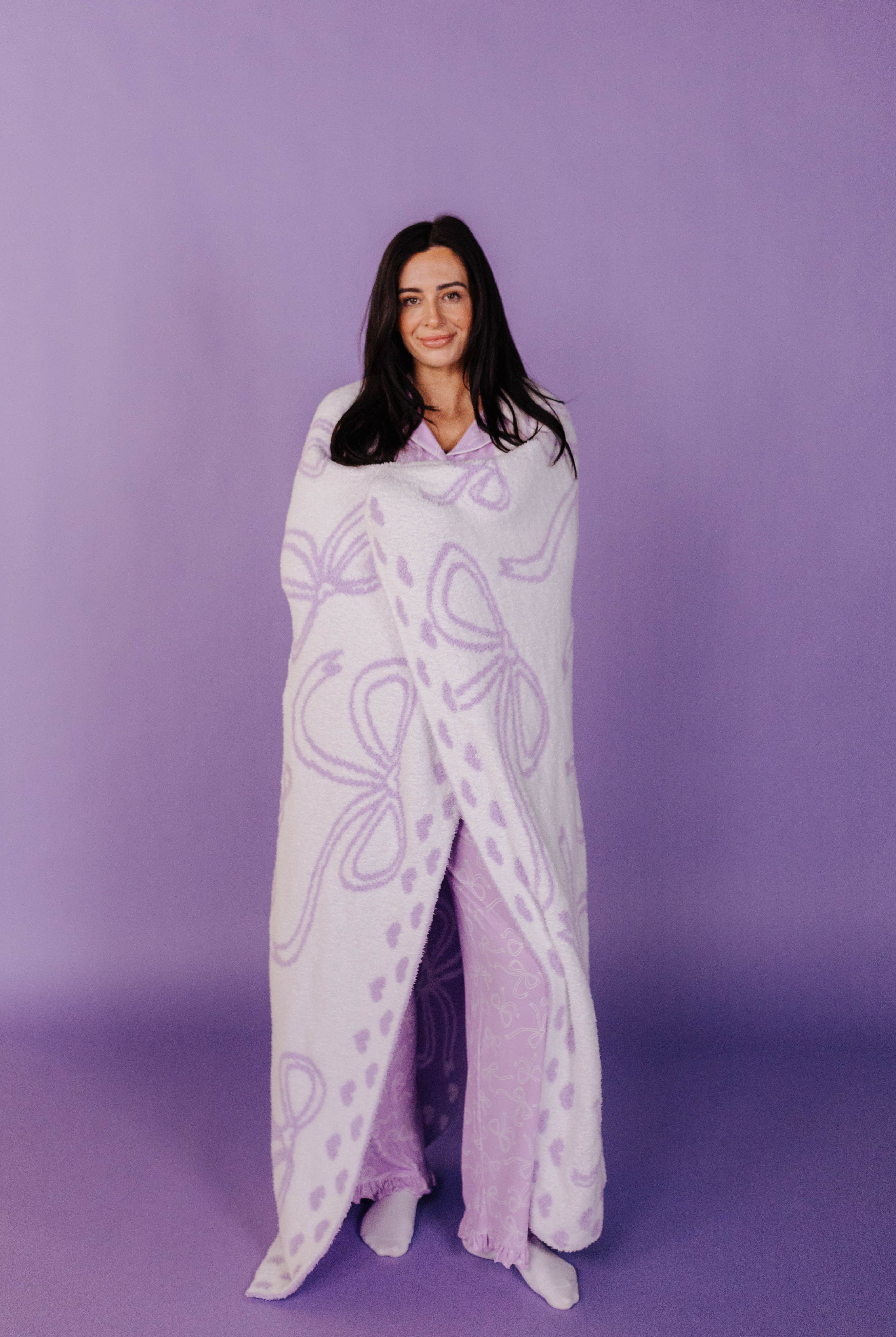 Woman wrapped in a purple bow patterned blanket against a purple background