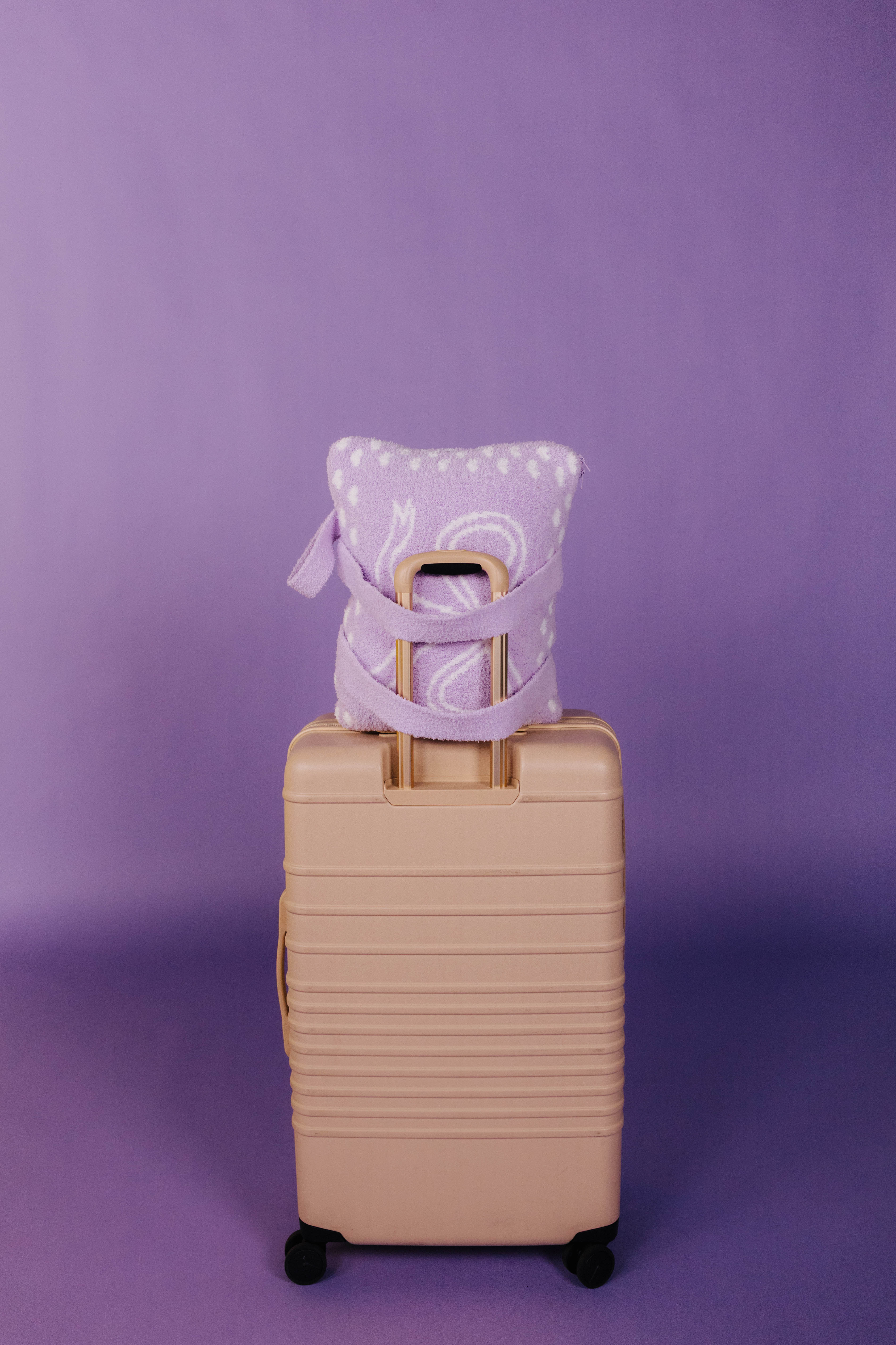 Beige suitcase with a purple quillow and strap on a purple background
