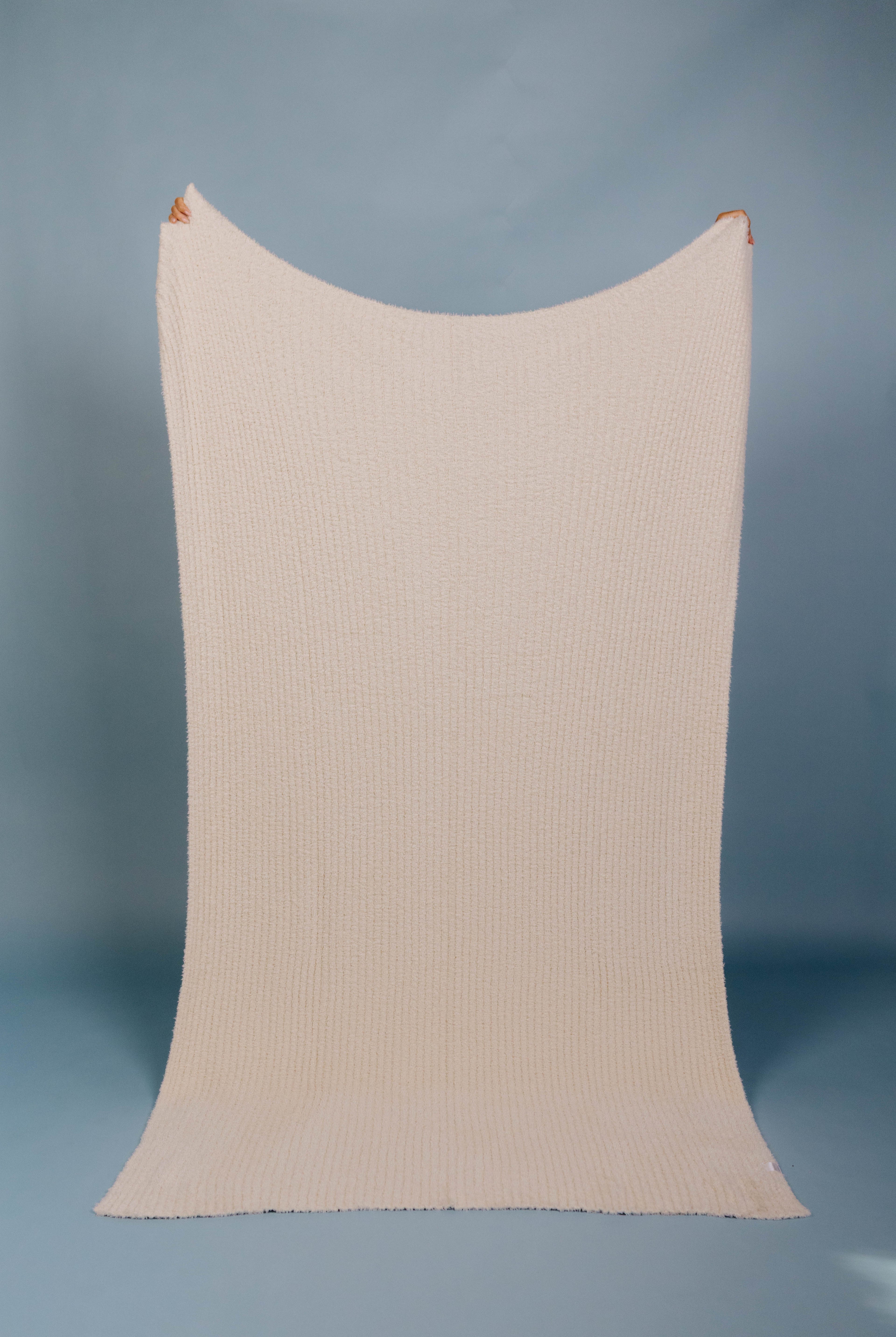 Beige ribbed blanket being held up on a blue background
